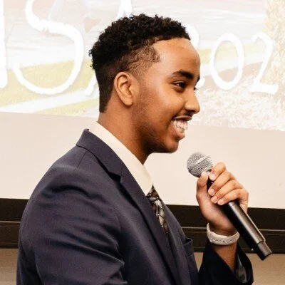 Last Mile awardee Mohamed M. in a suit, speaking into a microphone