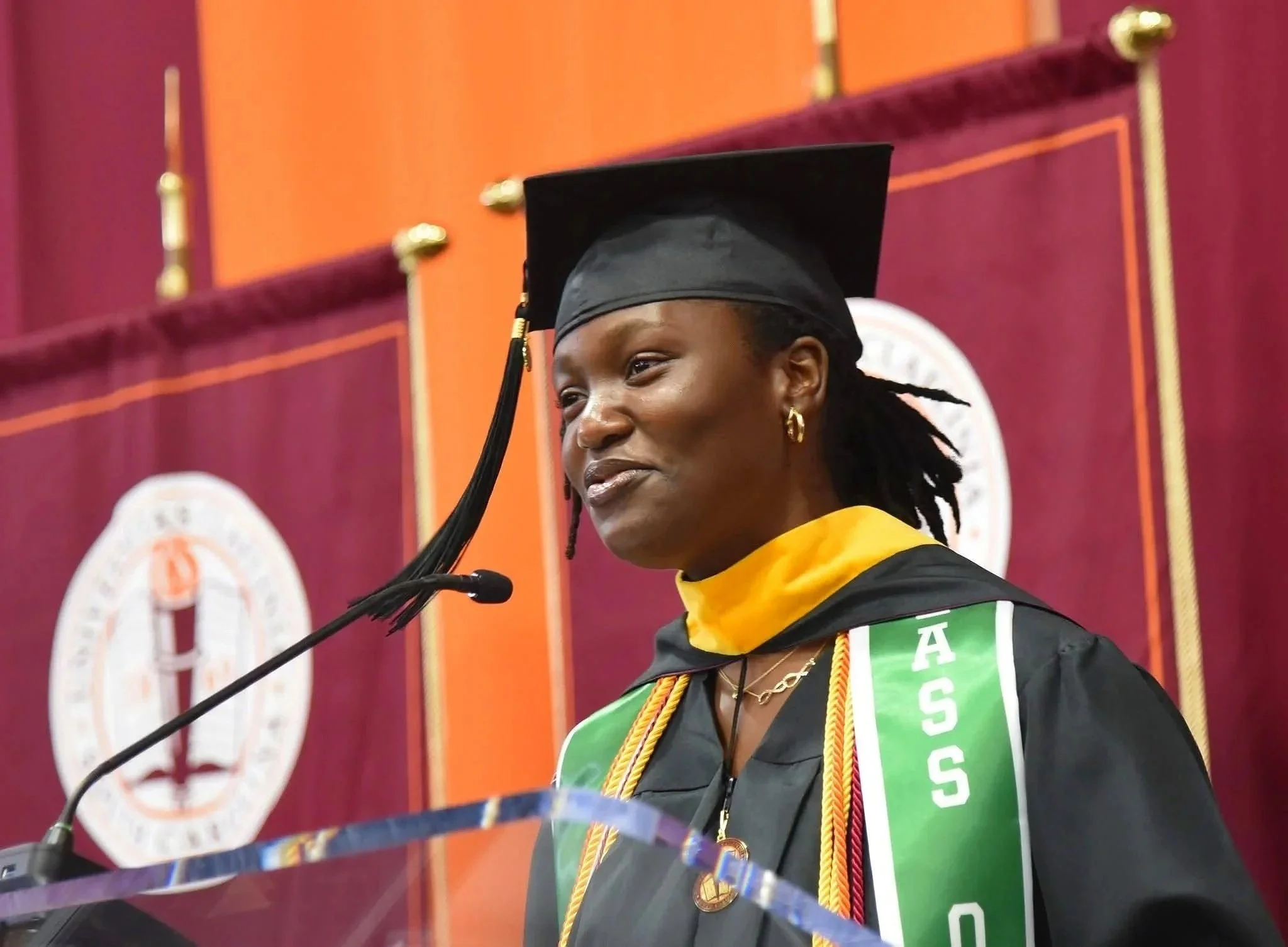 Last Mile awardee Oreoluwa A. in cap and gown speaking at a commencement podium
