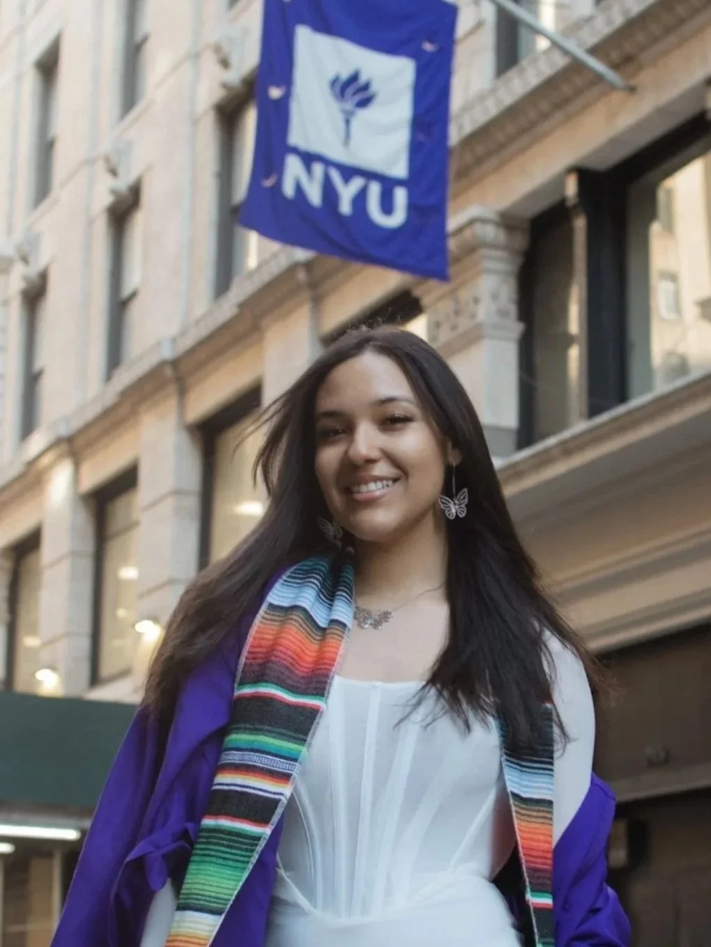 Last Mile awardee Estela B. on graduation day in front of an NYU flag
