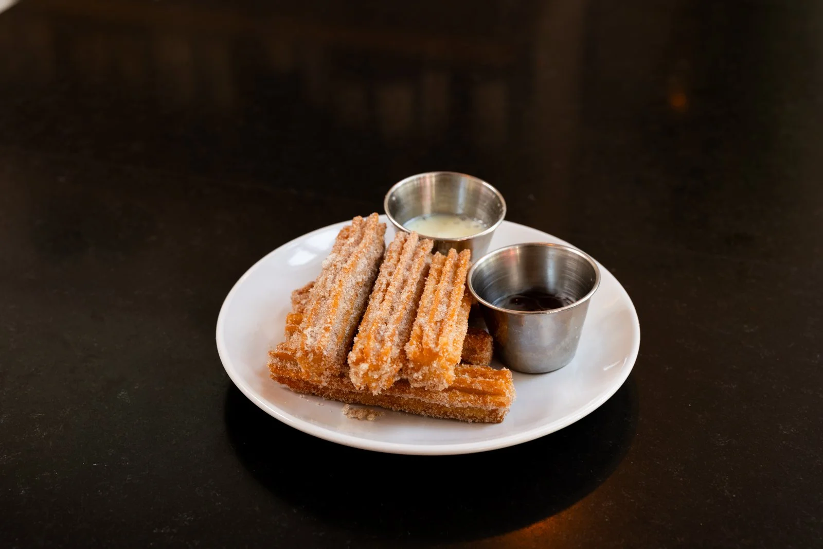 Plate with fried churros served with two dipping sauces on a black surface.