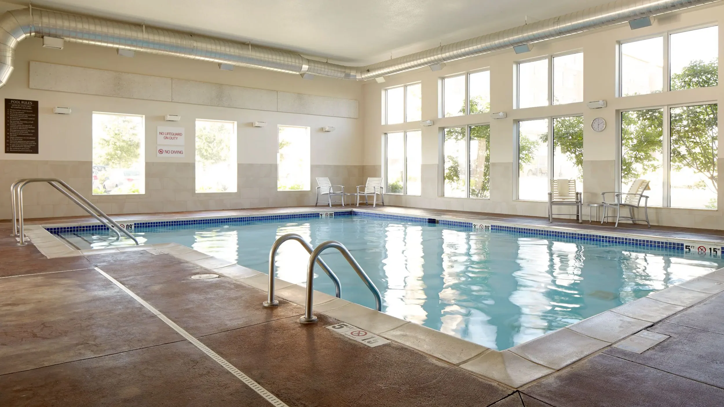 Indoor swimming pool with large windows, metal handrails, lounge chairs, and signs on the wall.