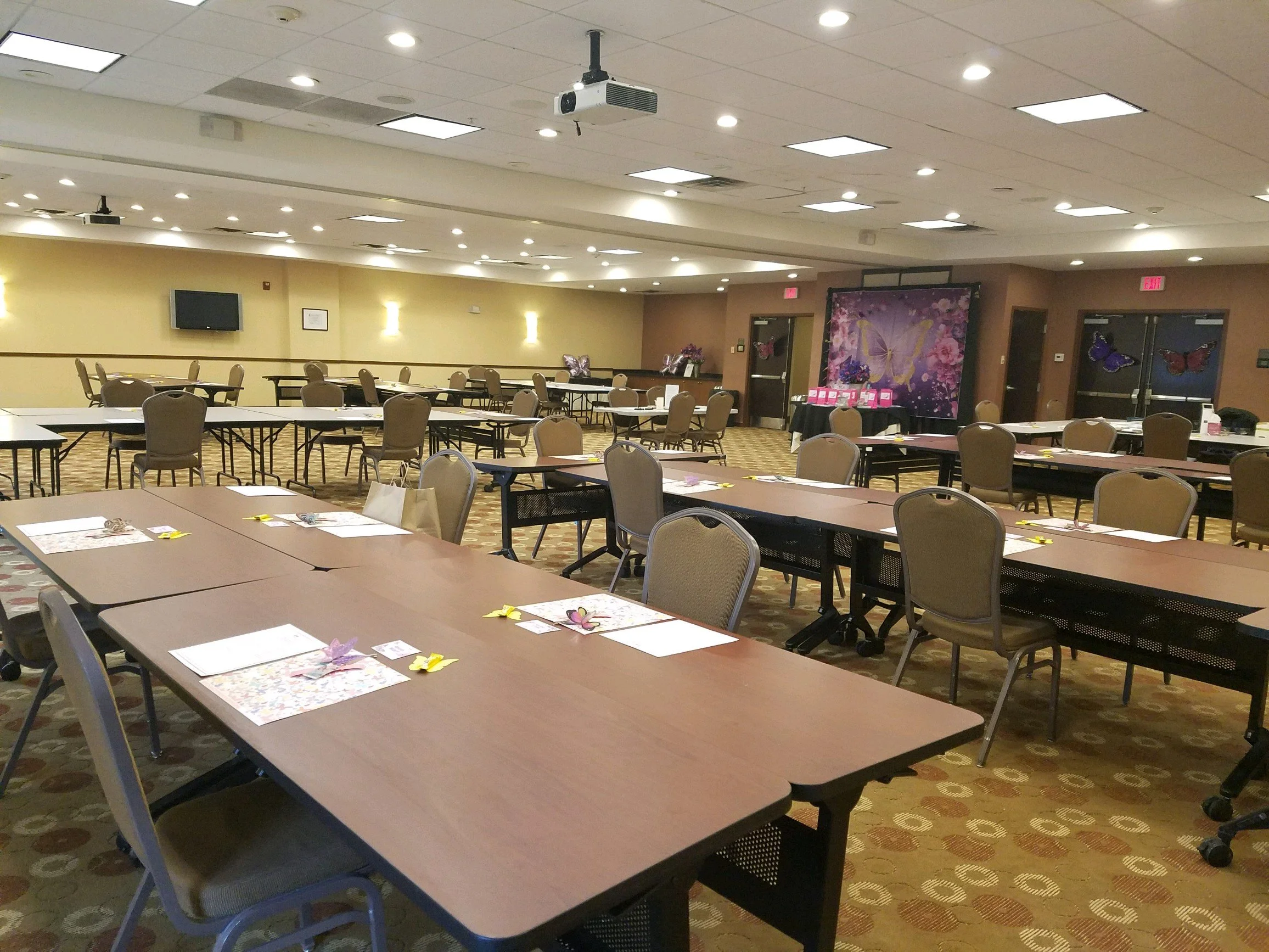 A spacious conference room with arranged tables and chairs, decorated with butterfly-themed table settings and wall decor.