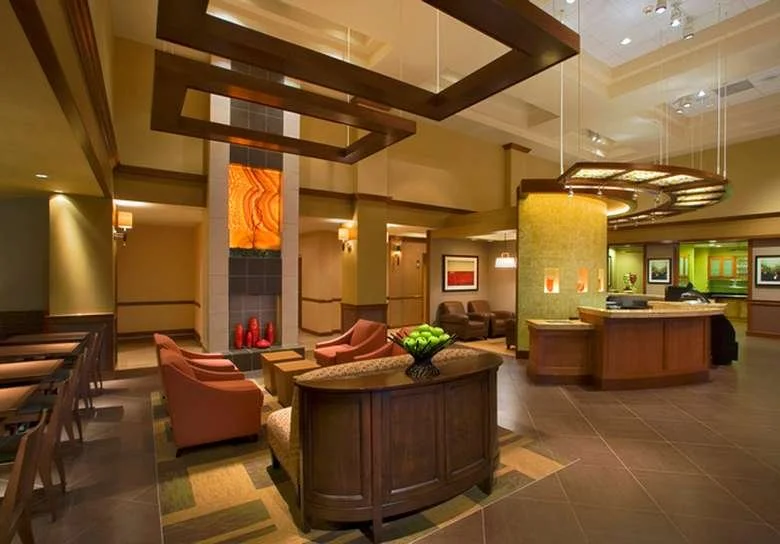 A hotel lobby with a reception desk, seating area with armchairs and a sofa, decorative lighting, and artwork on the walls.