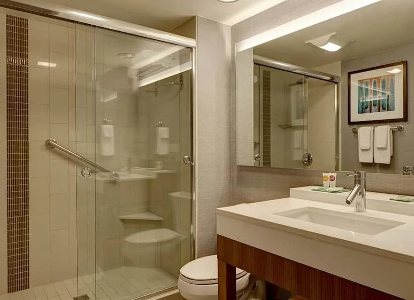 Bathroom with a glass shower, white sink with a wooden vanity, mirror, framed artwork, and towels hanging on a rack.