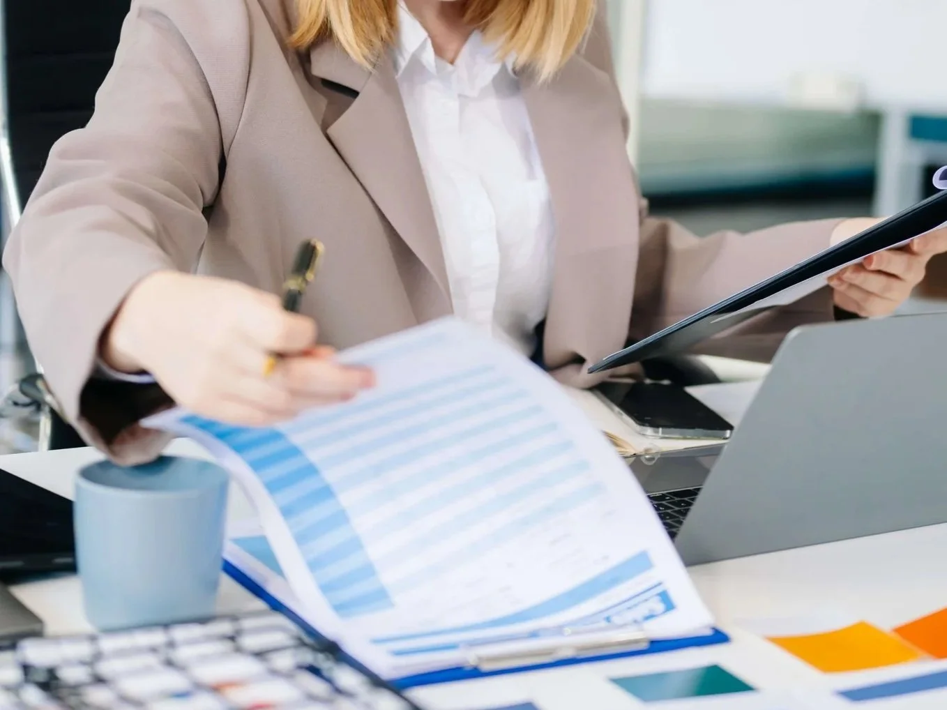 Businesswoman working at her desk with documents, a coffee mug, a laptop, a smartphone, and an electronic tablet.