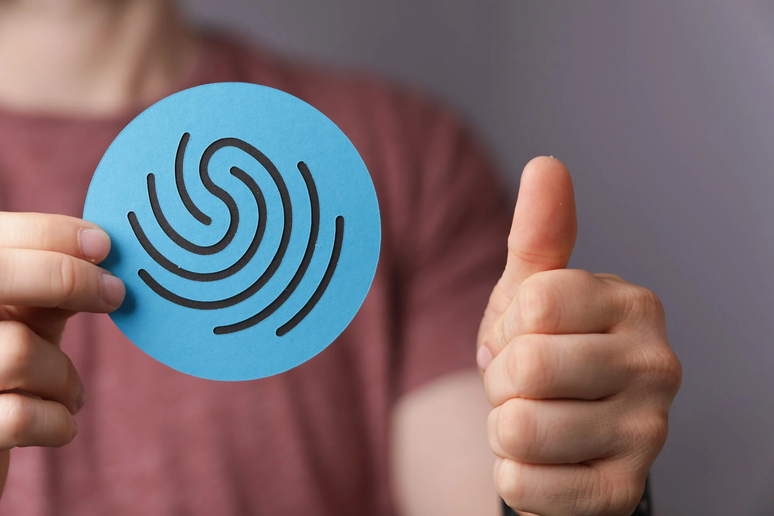 Person holding up a blue circular paper with black fingerprint pattern, giving a thumbs up.