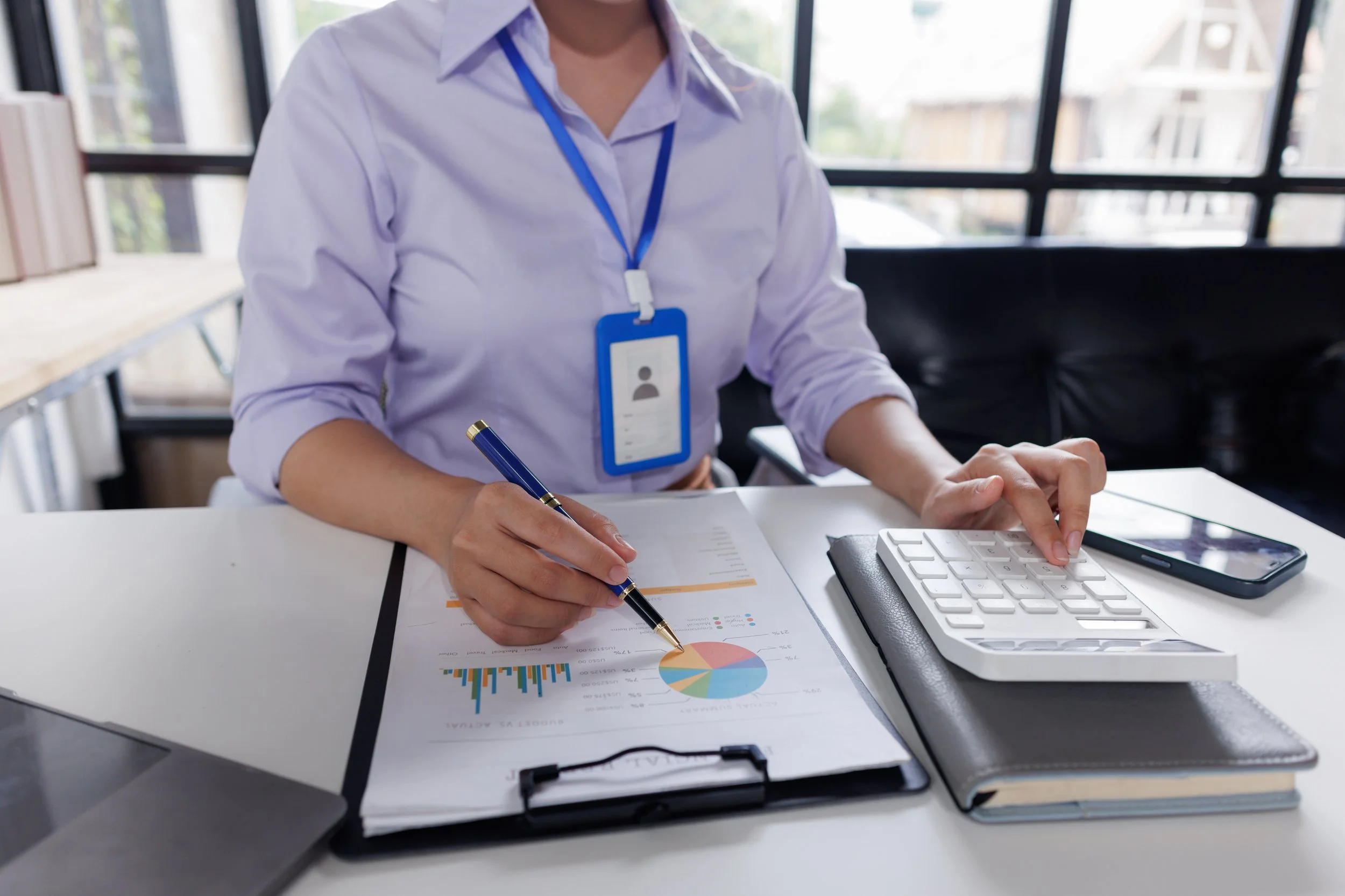 Person working at a desk with a pen, calculator, smartphone, and financial documents showing charts and graphs.