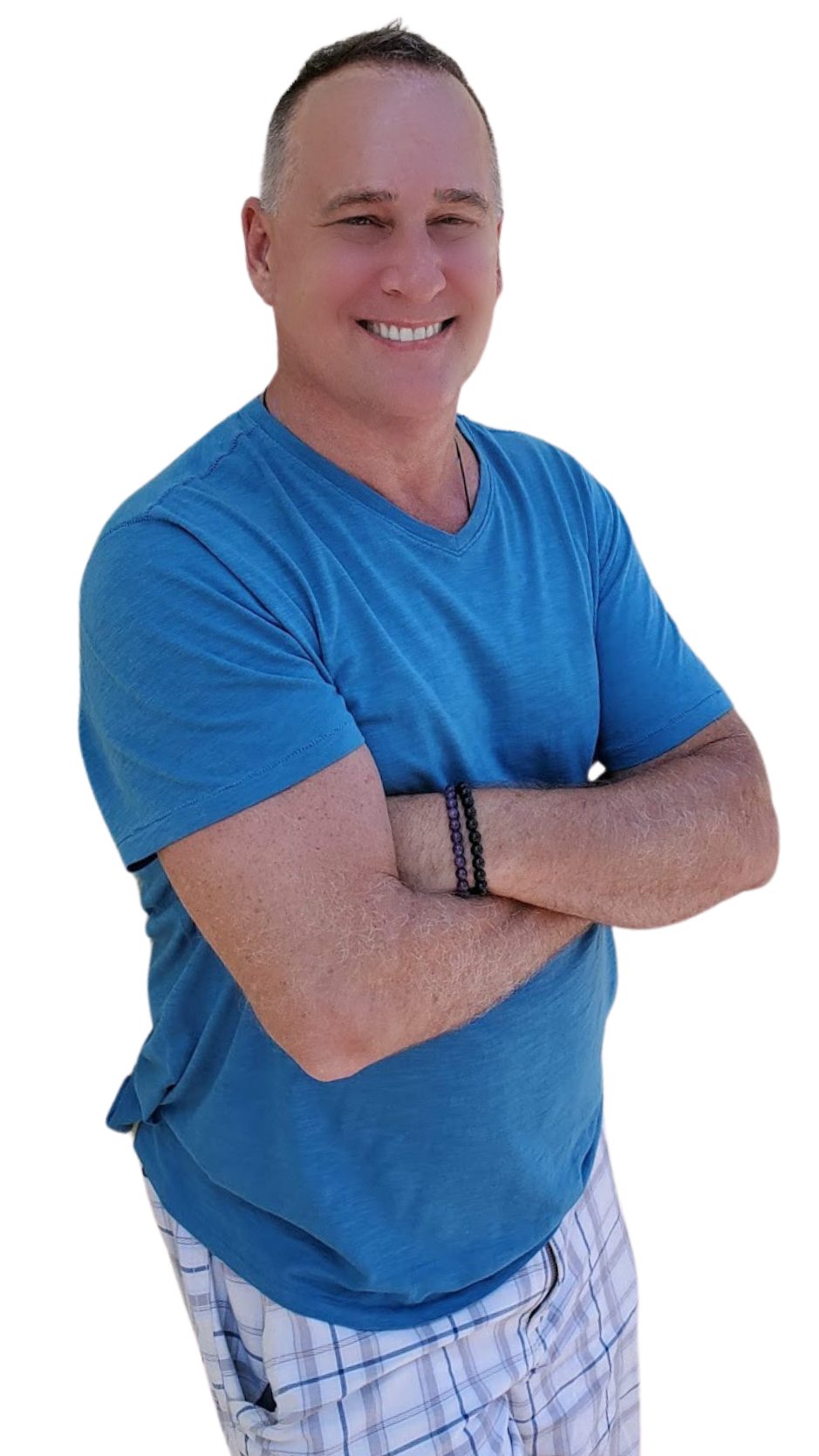 A man smiling with arms crossed, wearing a blue T-shirt and plaid shorts, standing outdoors.