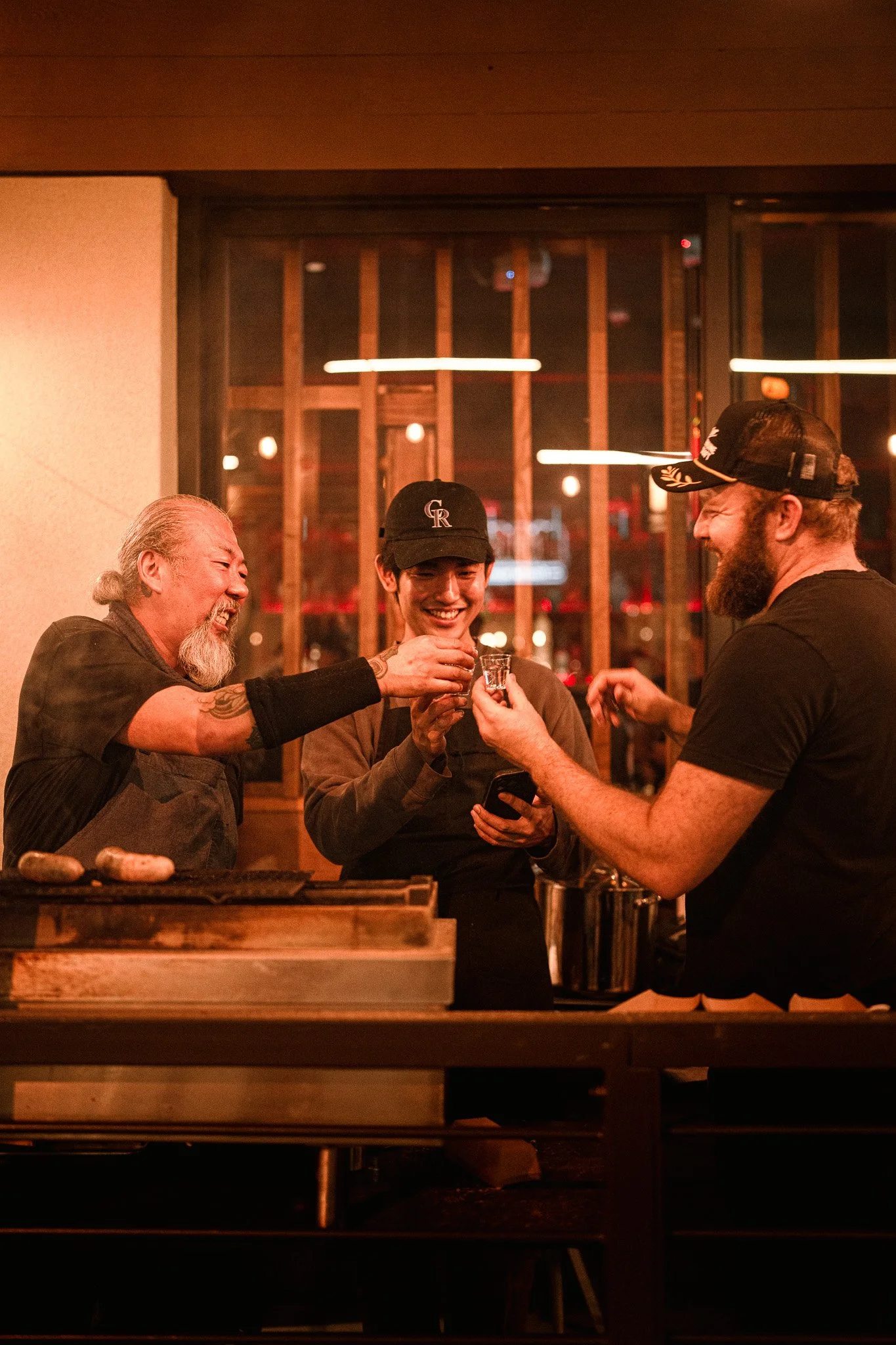 Three men enjoying a shot of alcohol together inside a restaurant or bar at night, smiling and having fun.