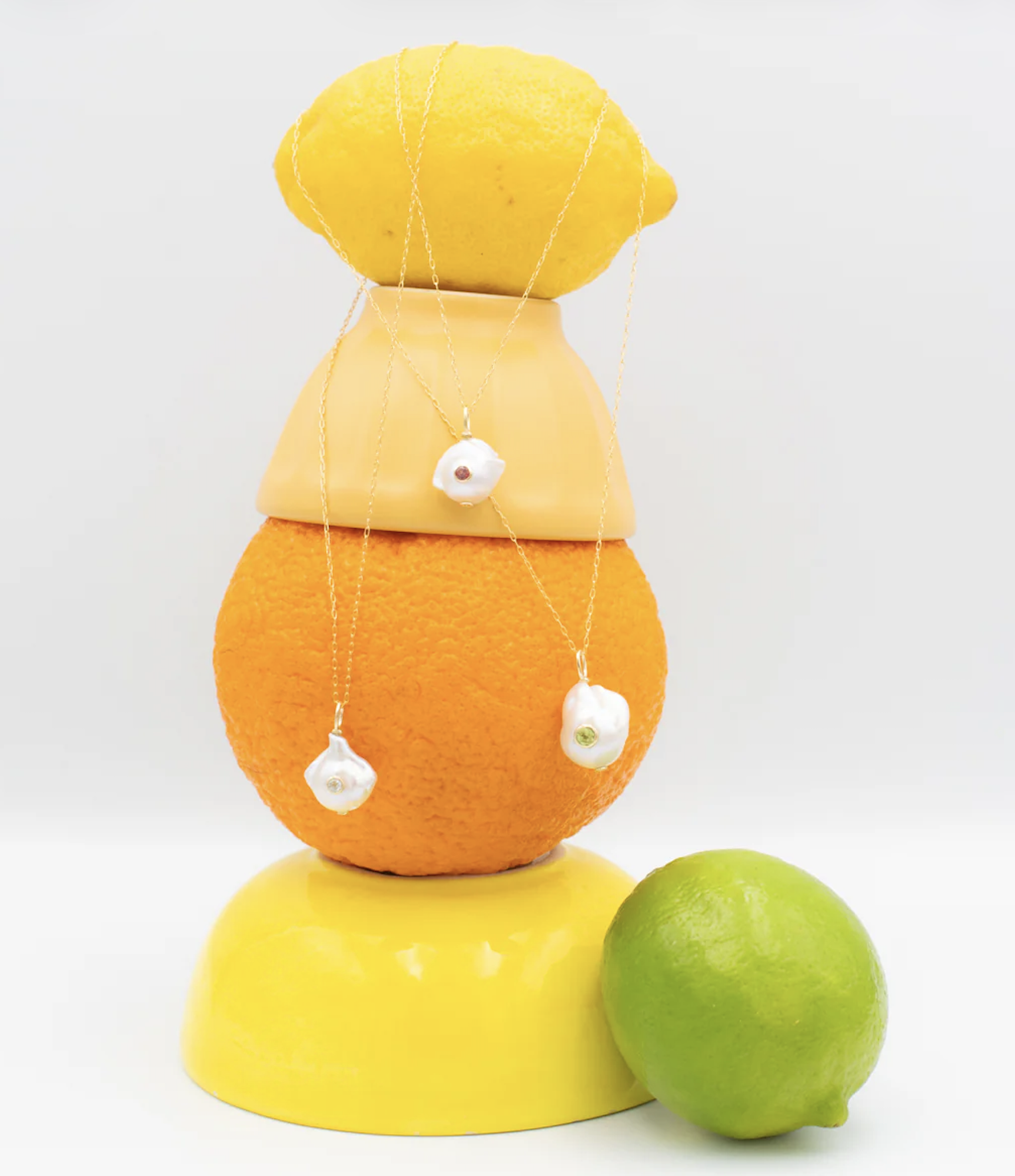 Stacked citrus fruits including lemon, orange, and lime with jewelry necklaces draped over the top lemon.