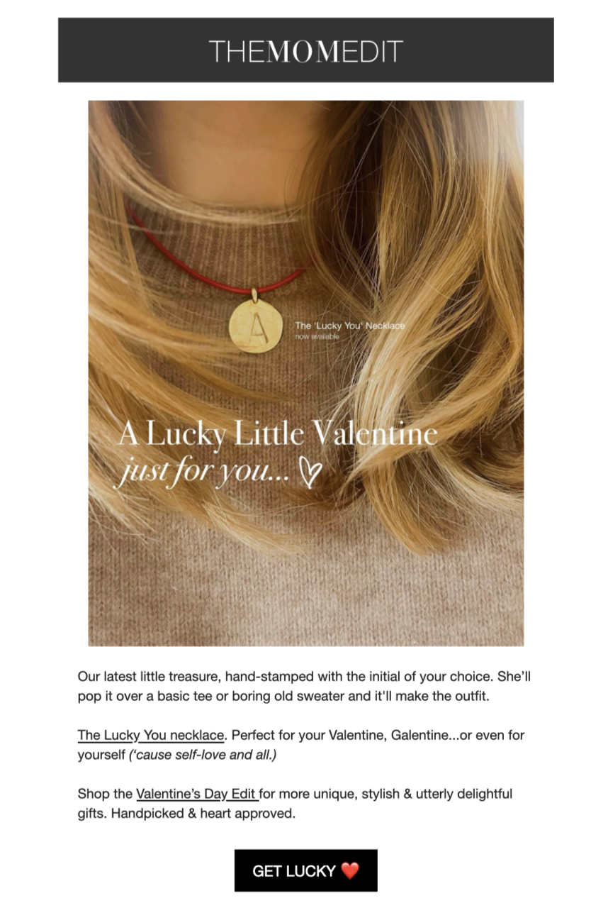 Close-up of a woman wearing a beige turtleneck and a gold necklace with a round disc pendant engraved with the letter A, advertising the 'Lucky You' necklace for Valentine's Day.