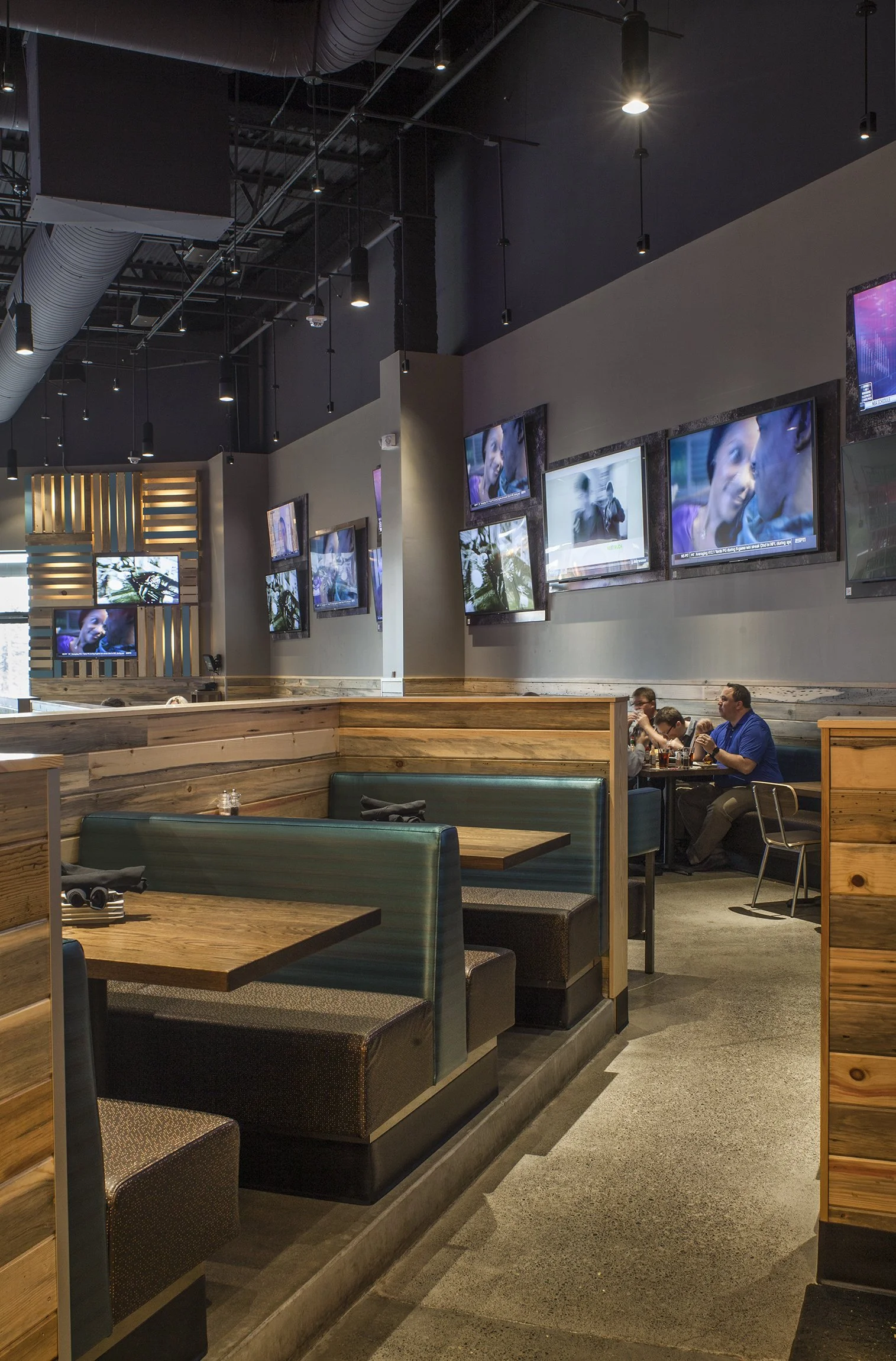 Interior of a sports bar or restaurant with booths, multiple wall-mounted TVs showing various programs, and customers seated at tables.