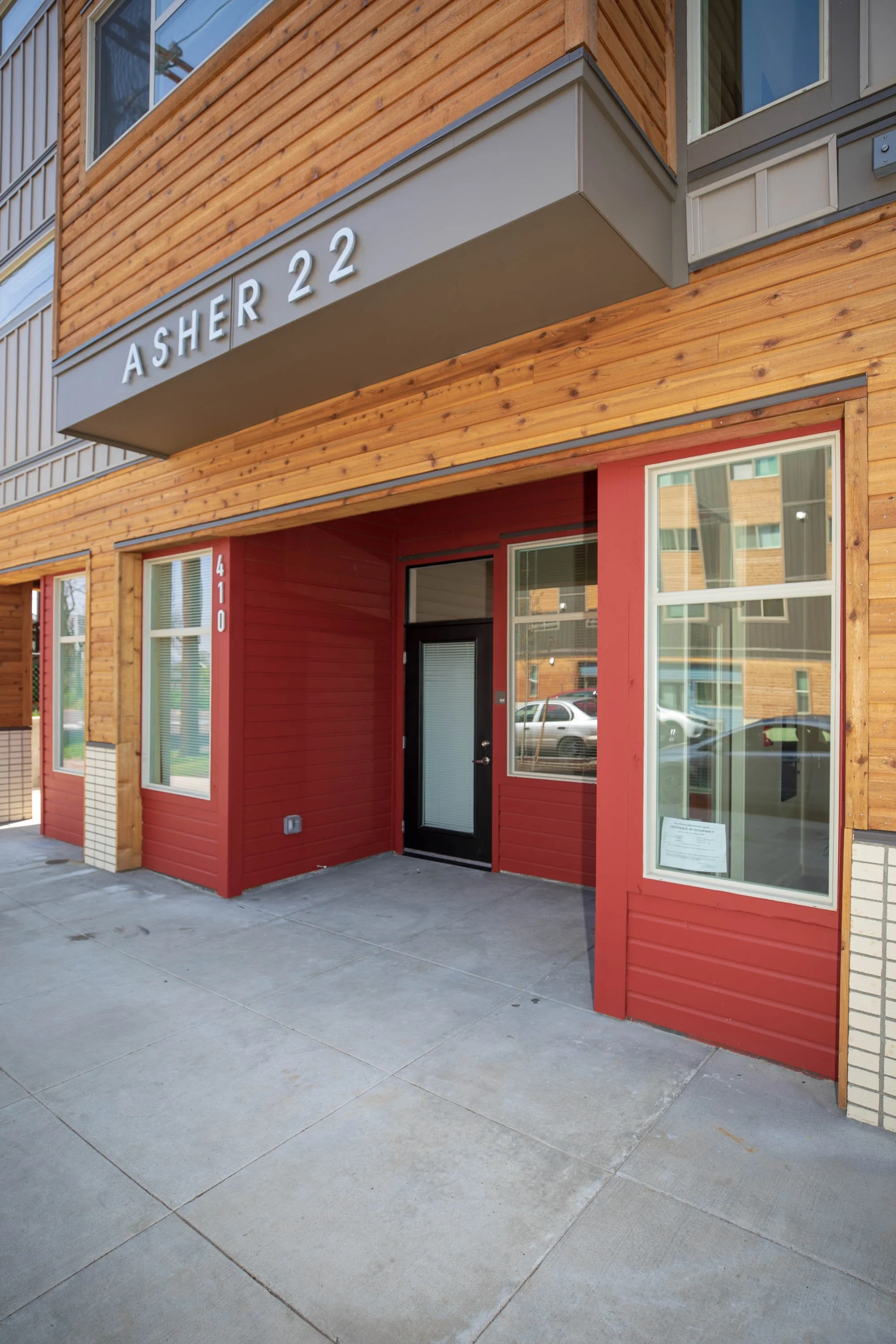Exterior of a modern building with a red facade, wood siding, large windows, and a black door, located at 410.
