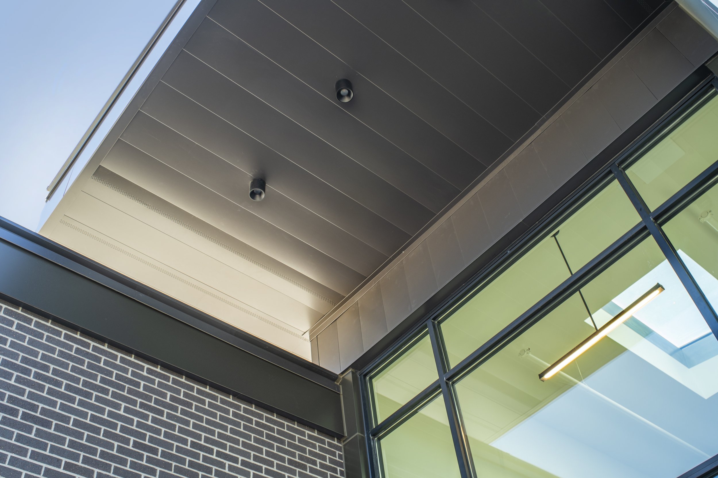 Close-up of a modern building's awning with black brick wall, glass window, and ceiling lights.