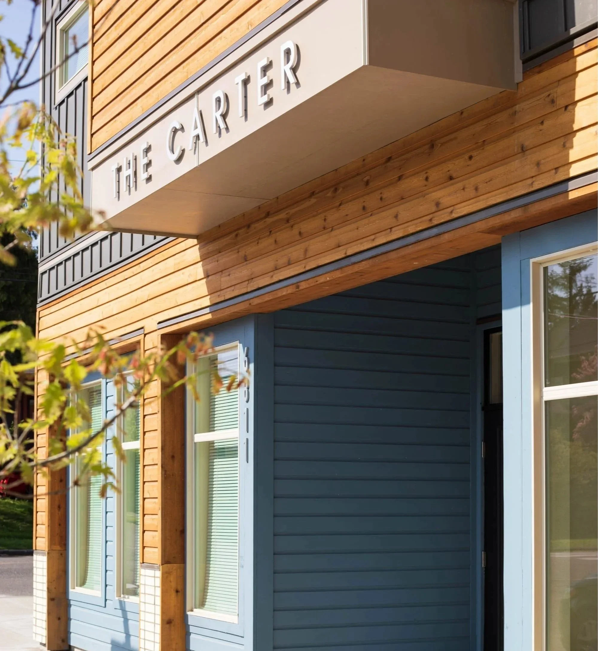Exterior of a modern building with wood and blue siding, displaying the sign 'The Carter' on a white panel above the entrance.