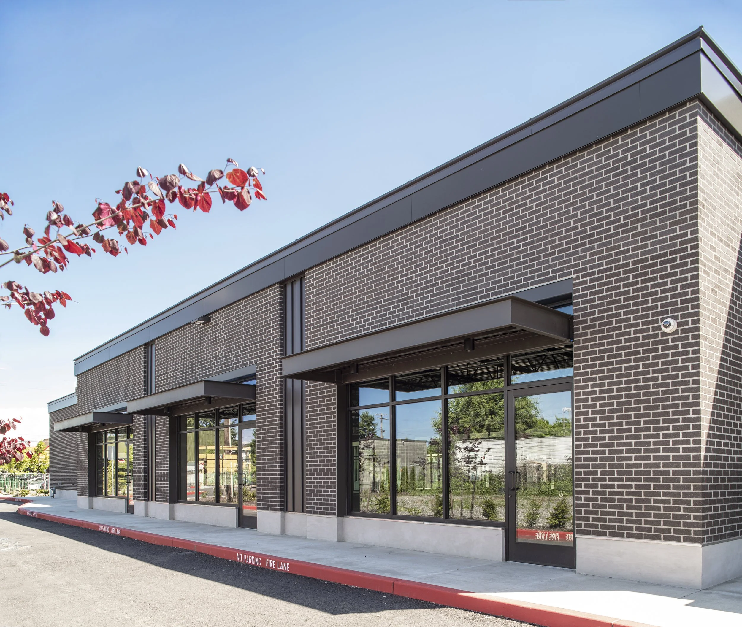 New commercial building with brick exterior, large glass windows, and a black awning, set against a clear blue sky.