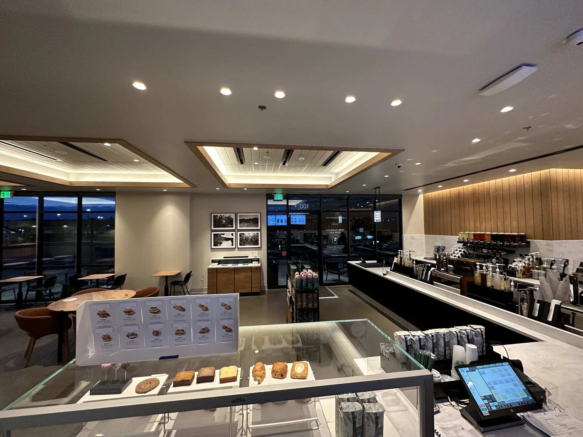 Interior of a modern coffee shop or cafe with a display case of baked goods, seating area, and a coffee counter with various coffee-making equipment.