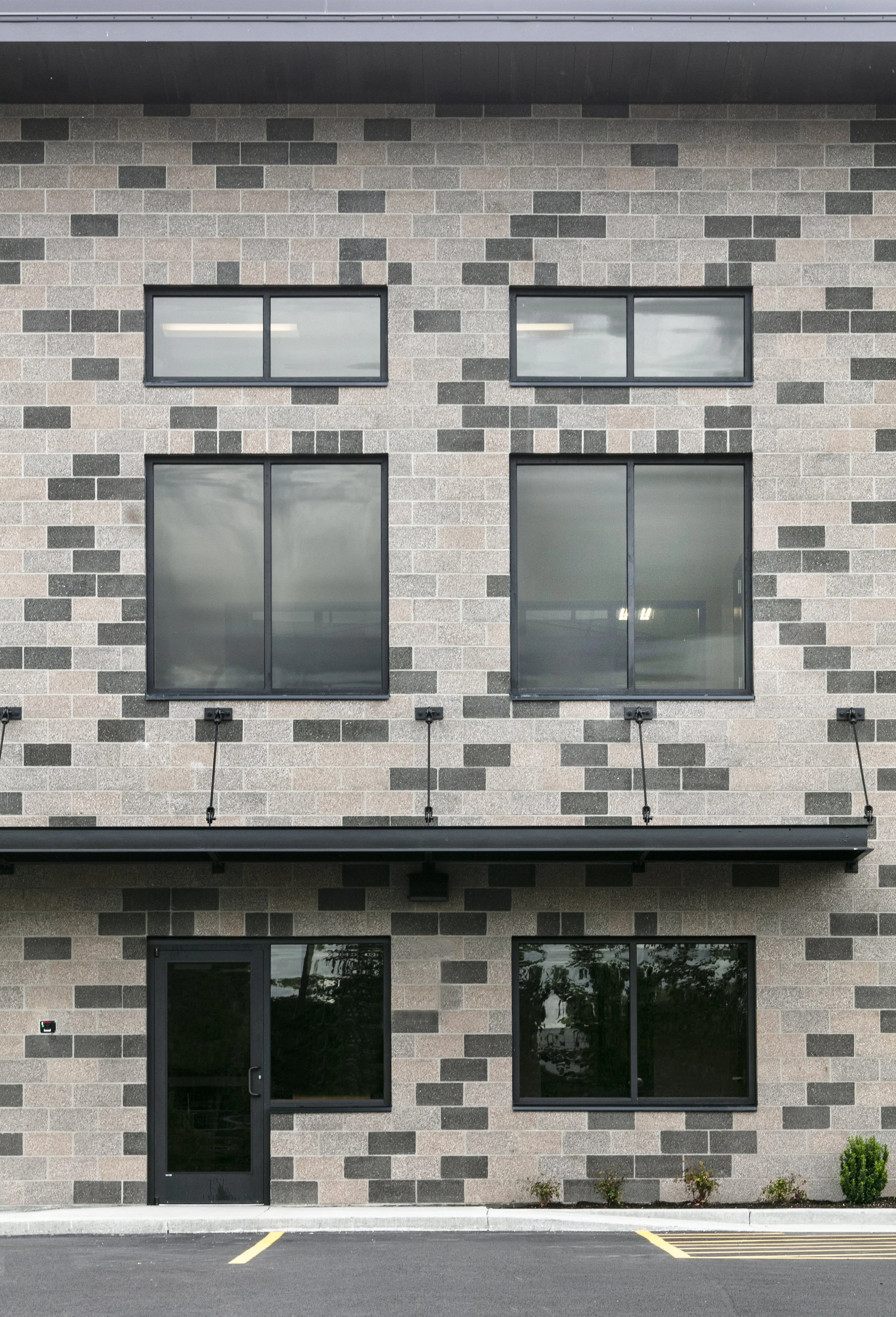 Front of a modern office building with a brick exterior, multiple black-framed windows, and a small parking area with yellow lines.