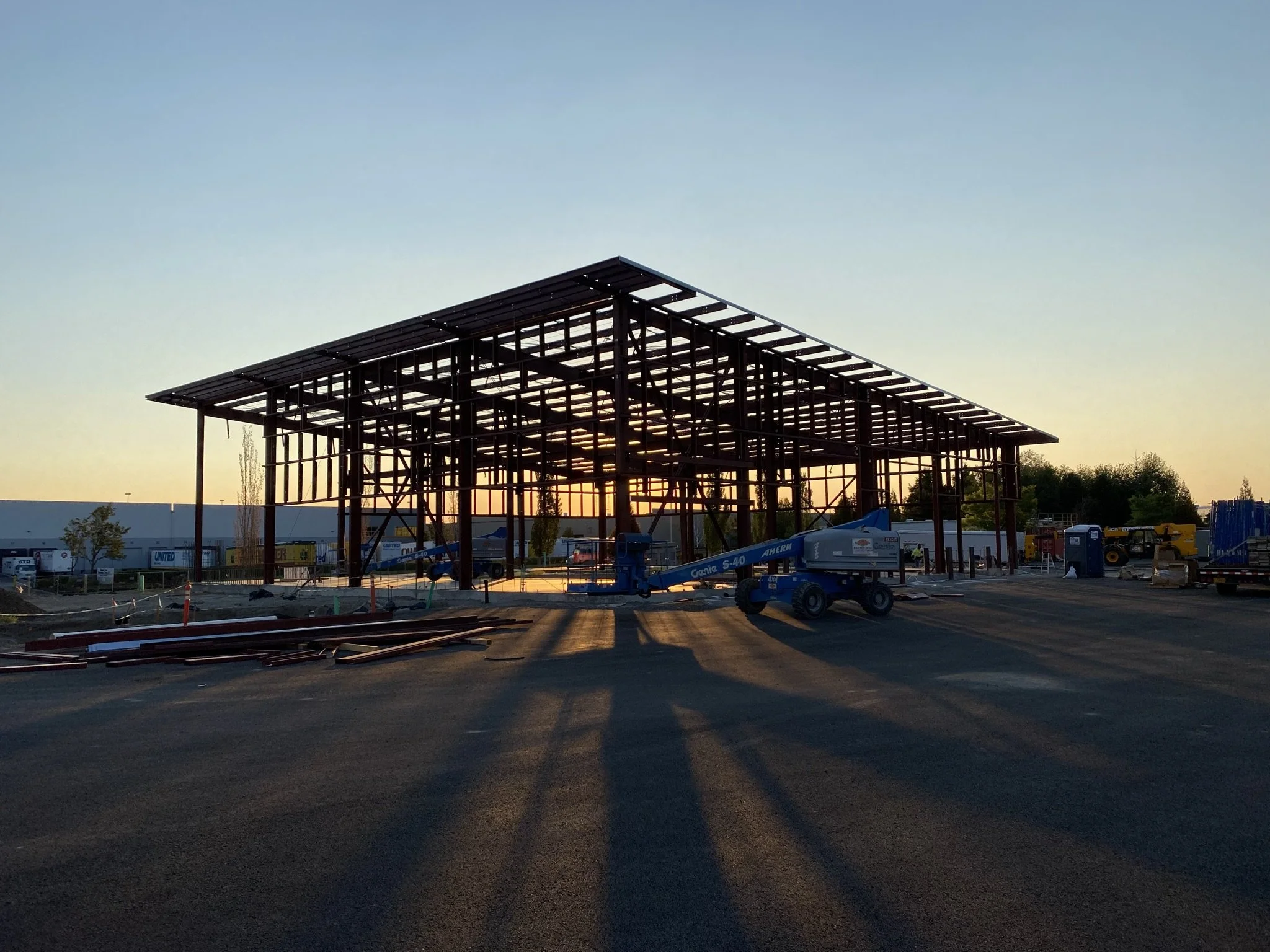 Construction site at sunset with a steel framework of a building and construction equipment on the ground.