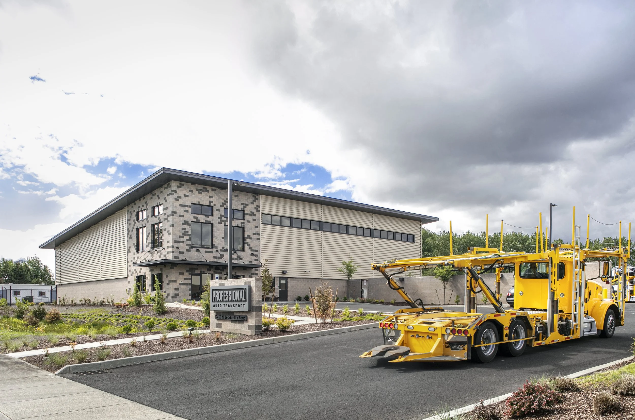 Modern commercial building with a yellow tow truck parked in front.