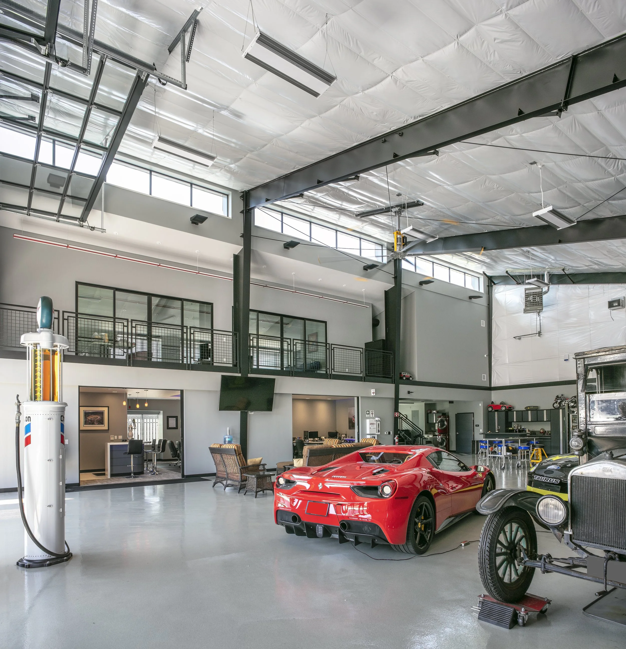 Interior view of a modern classic car and a red sports car parked inside a spacious garage or showroom with high ceilings, large windows, and industrial design elements.