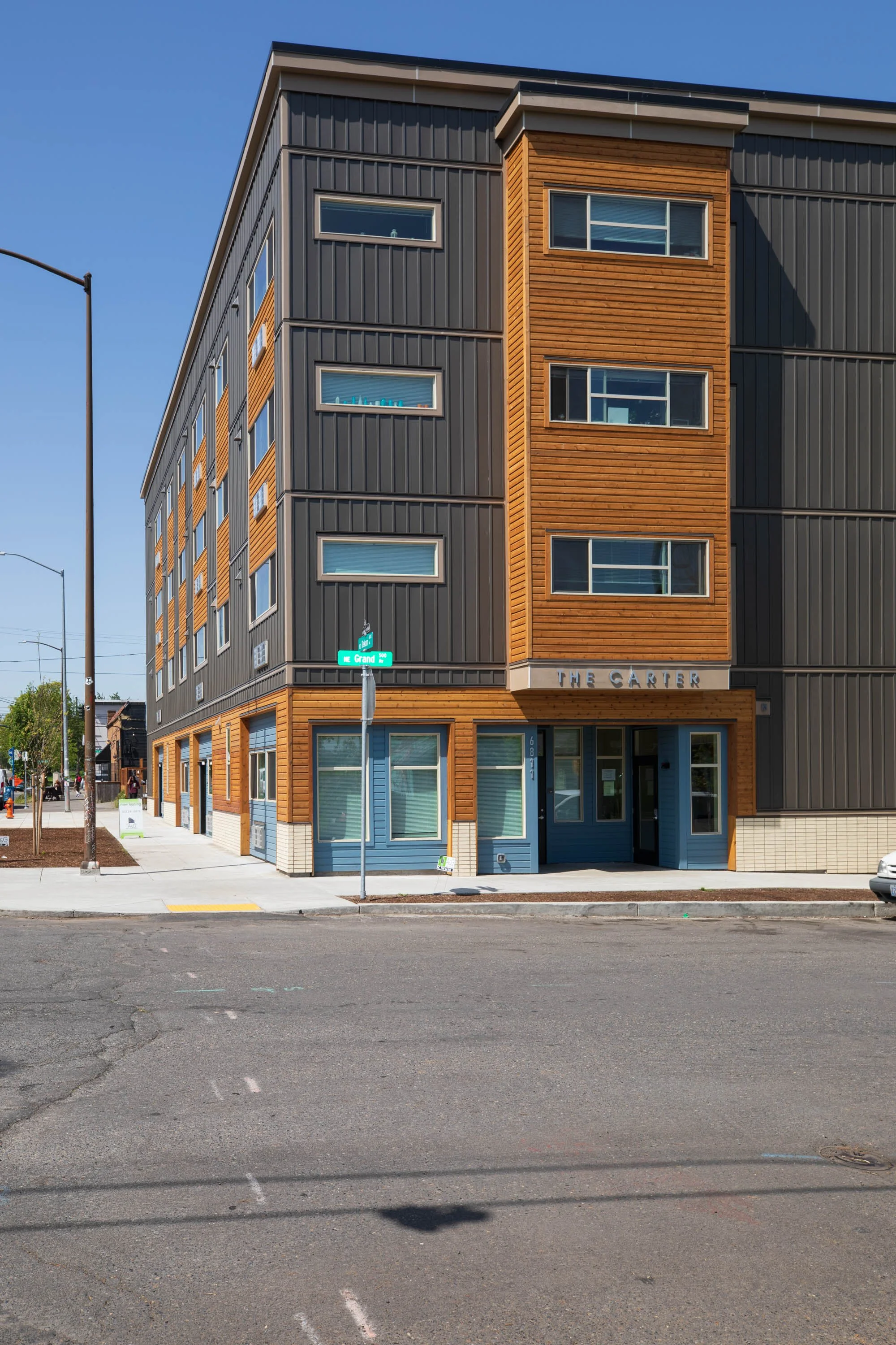A modern multi-story building with wood and metal siding on a city street corner, labeled 'The Carter,' with street signs and sidewalk visible.