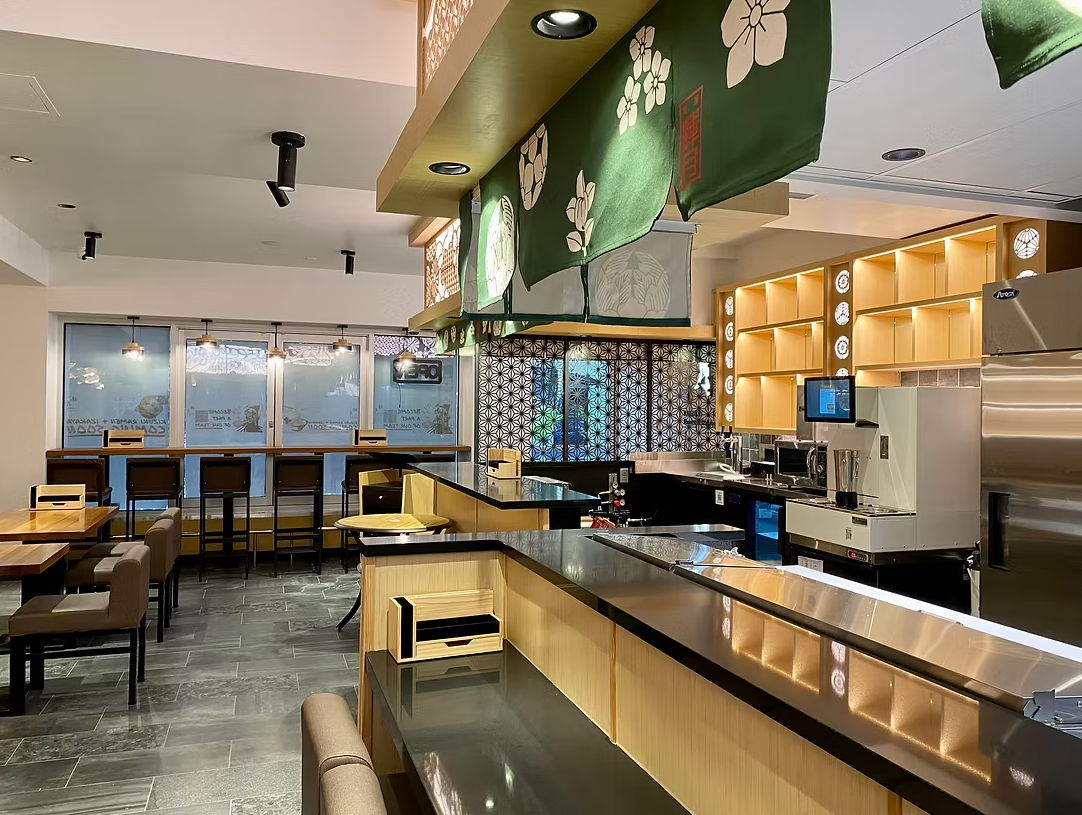 Interior of a modern restaurant or cafe with a counter, tables, chairs, and decorative hanging fabric with floral designs.