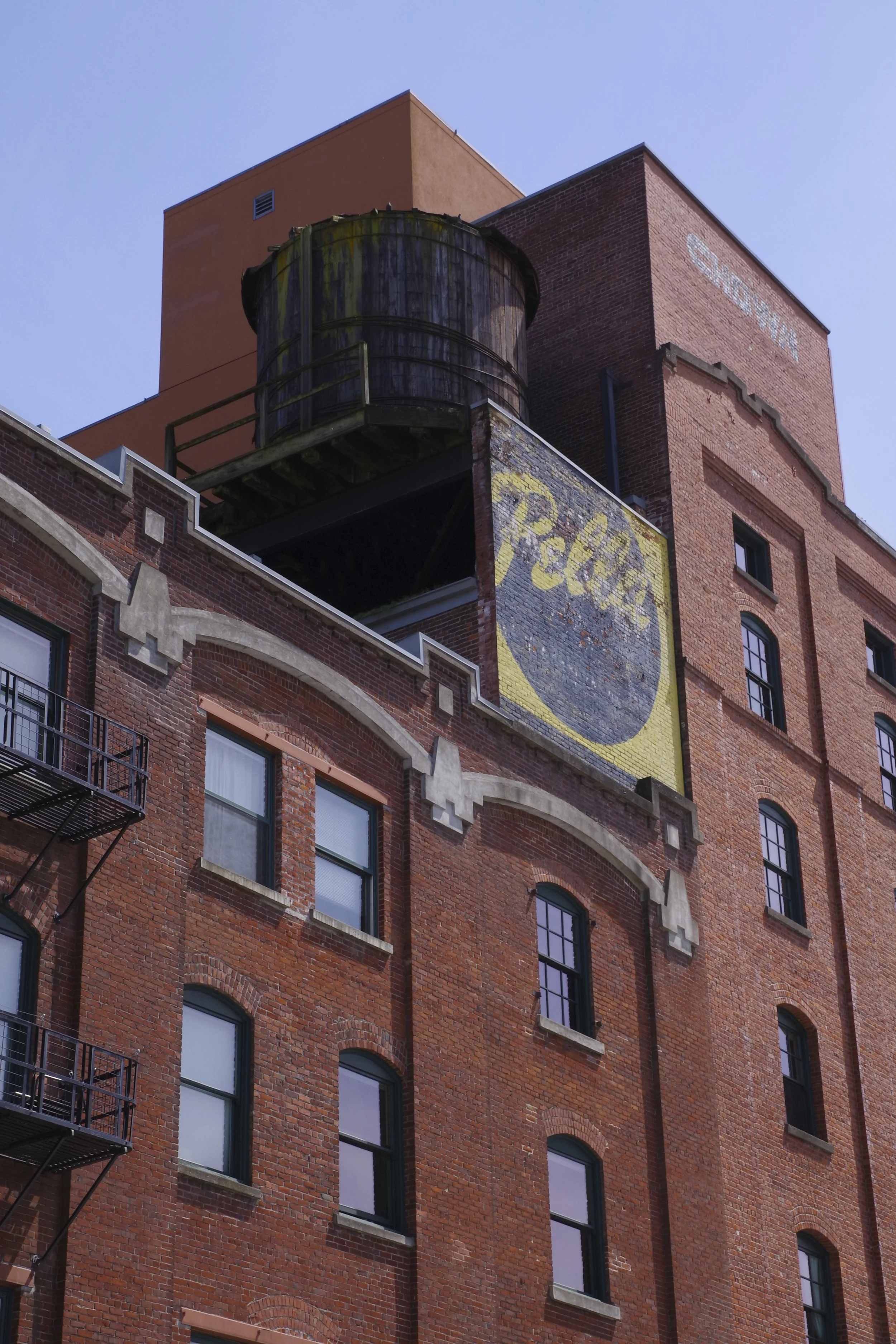 Close-up of a multi-story red brick building with several windows, an old water tank on a platform, and faded advertising signs on the upper part of the building.