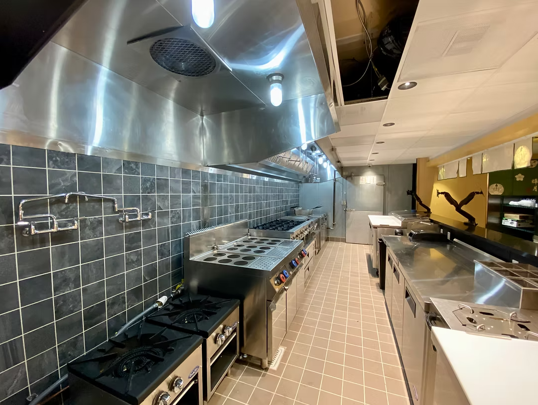 Commercial kitchen with stainless steel appliances, black tiled walls, gas stoves, and counters.
