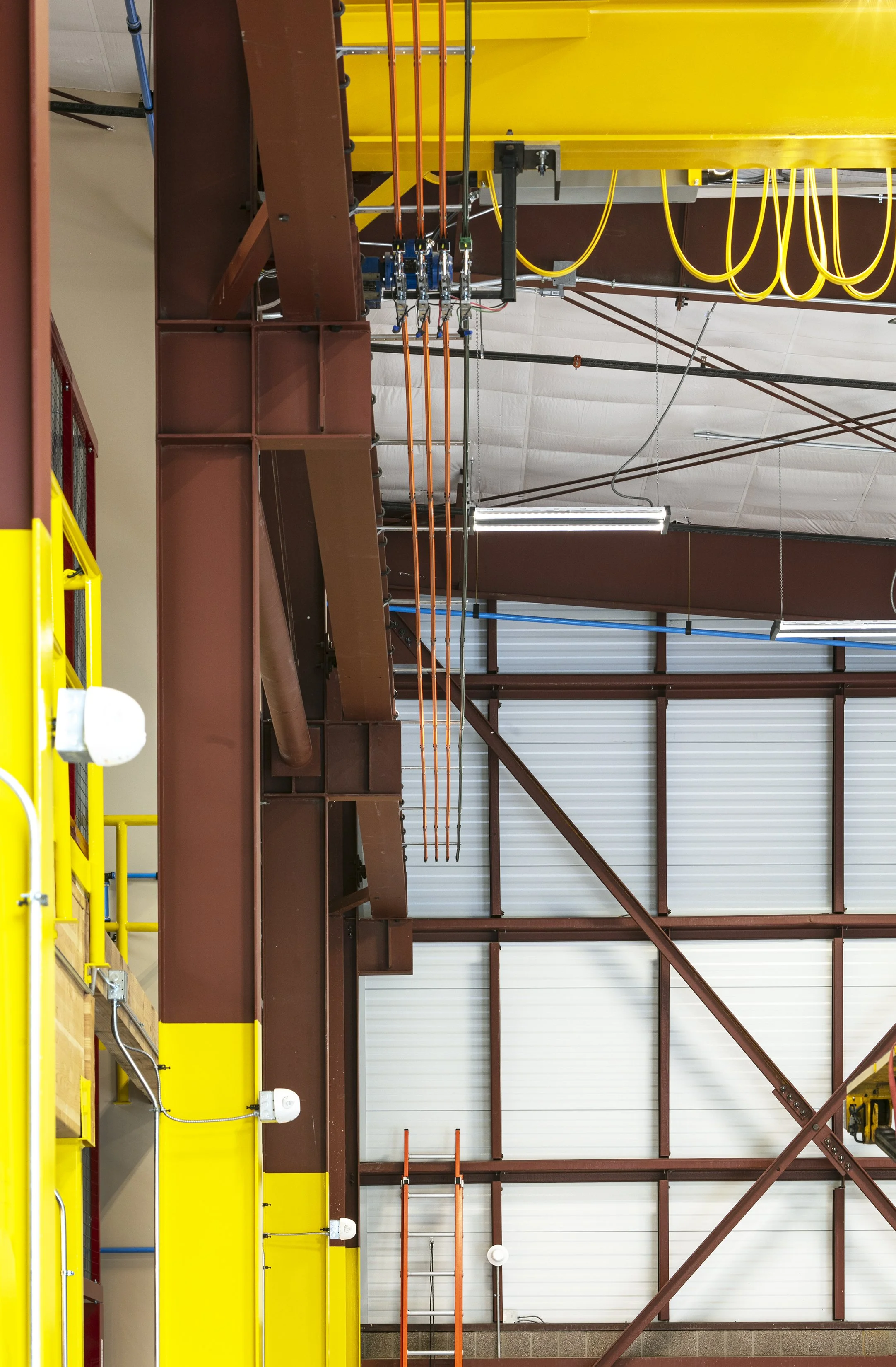 Interior view of an industrial or warehouse ceiling showing metal beams, pipes, and yellow safety cables hanging from the ceiling.