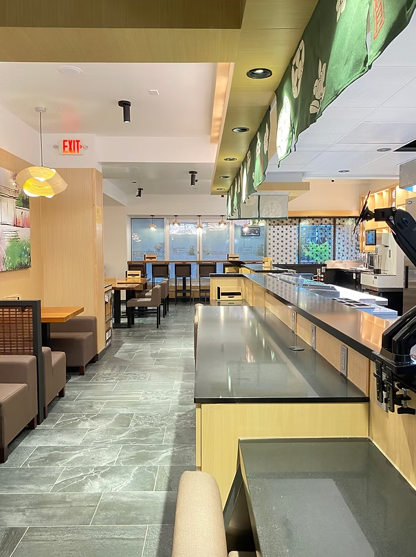 Empty restaurant with wooden tables and chairs, a counter with stainless steel surface, green hanging curtain, and windows showing the outside view.