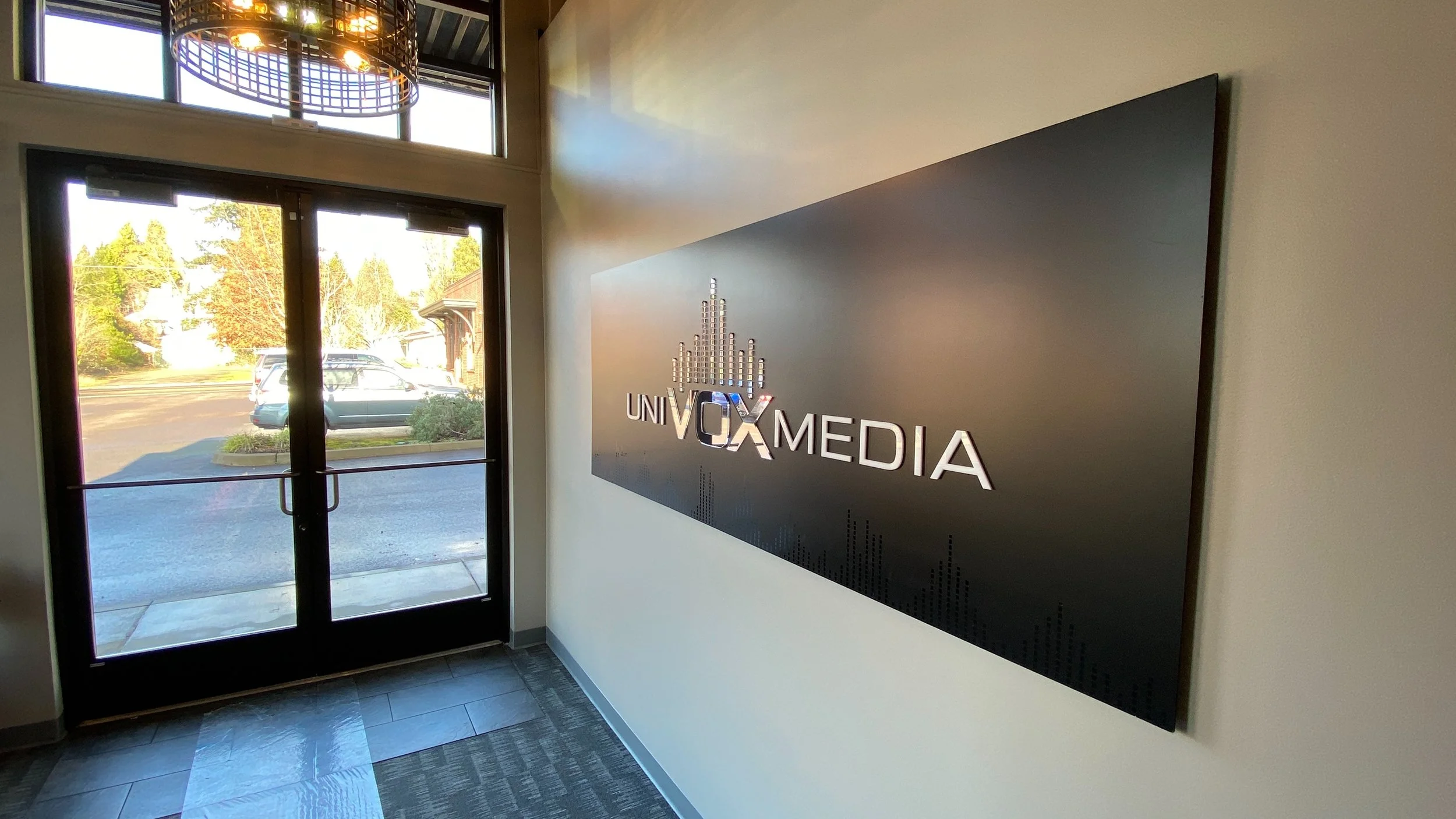 Interior lobby with windowed front door, a sign reading 'Univox Media', and a view of parked cars outside.
