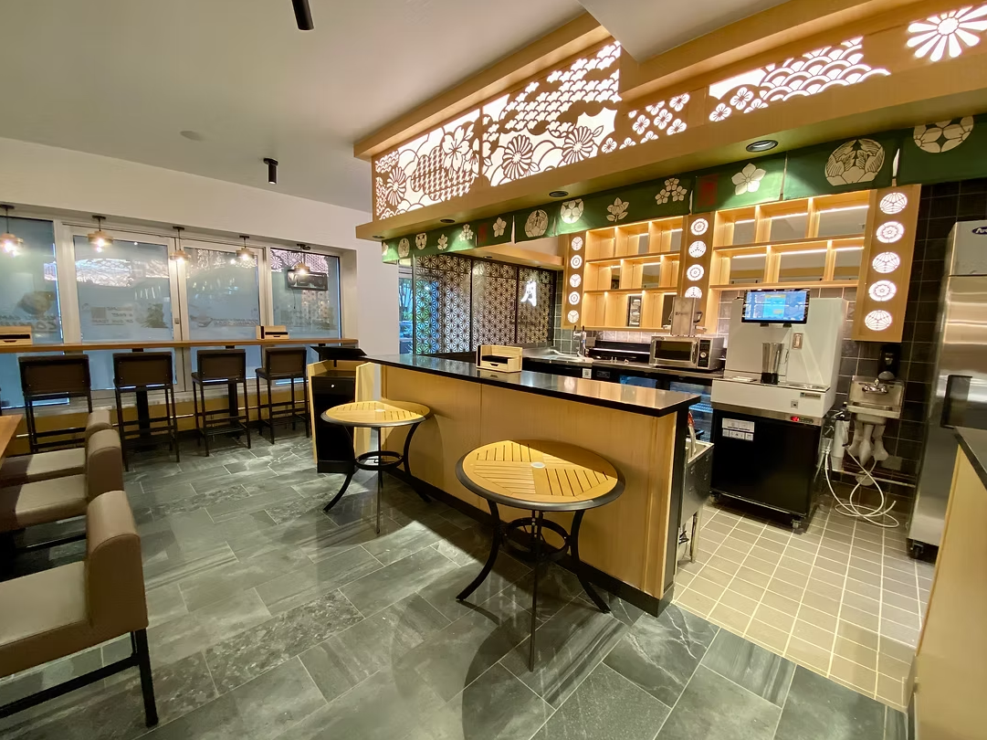 Empty cafe or restaurant with seating area, counter, and kitchen equipment, decorated with Japanese-inspired patterns and lighting.