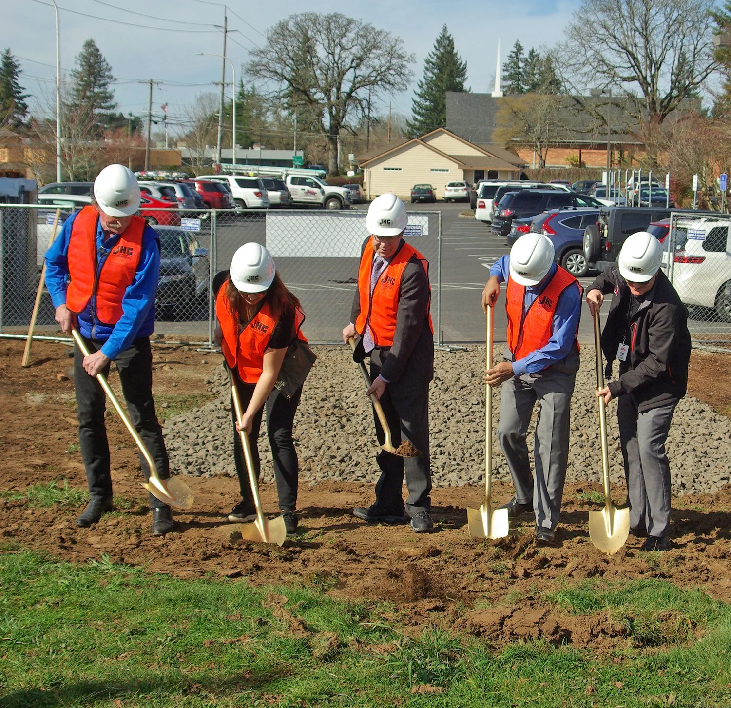 People wearing safety helmets and orange vests planting trees in a designated area.