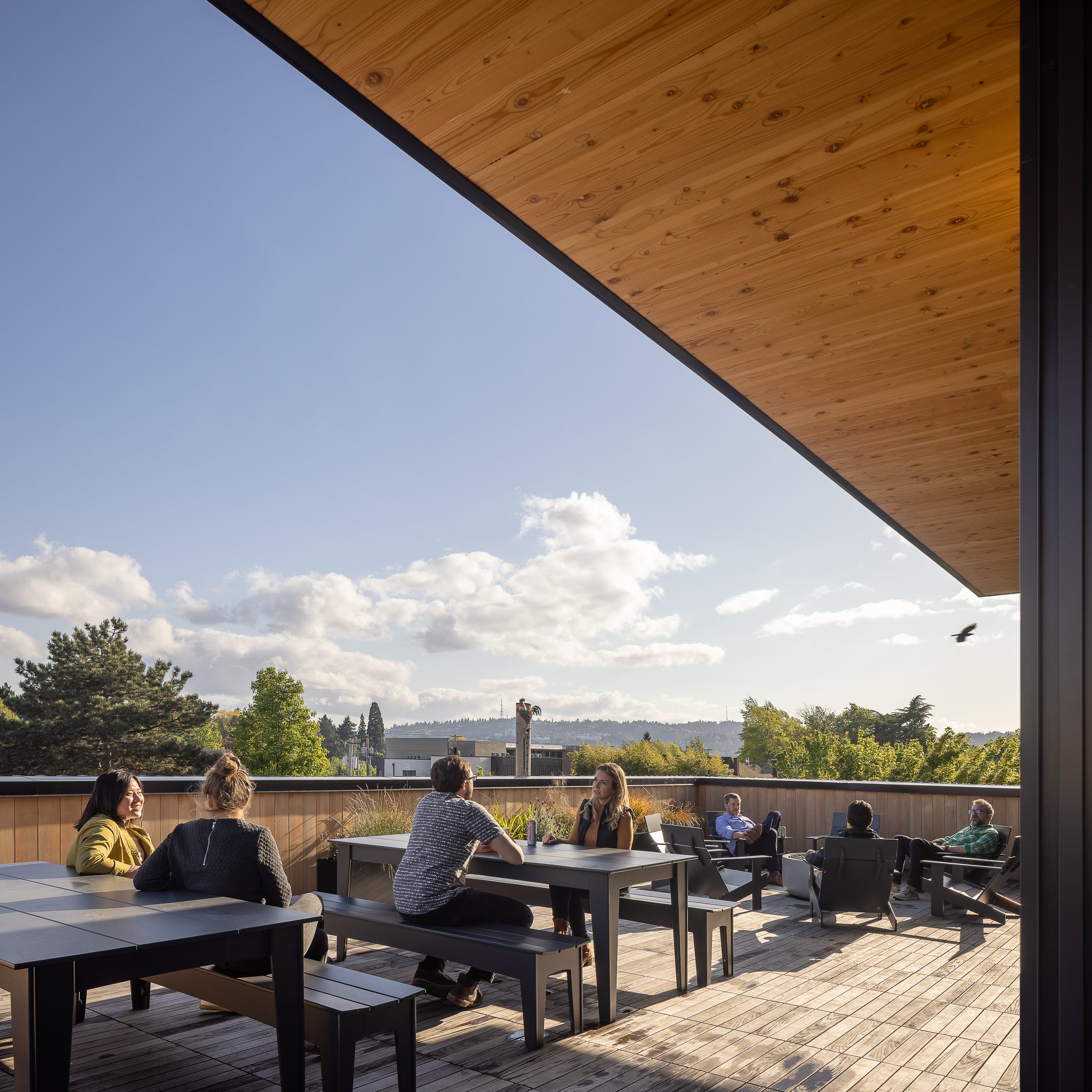 People sitting and chatting on a balcony patio with a view of trees and clouds in the sky.