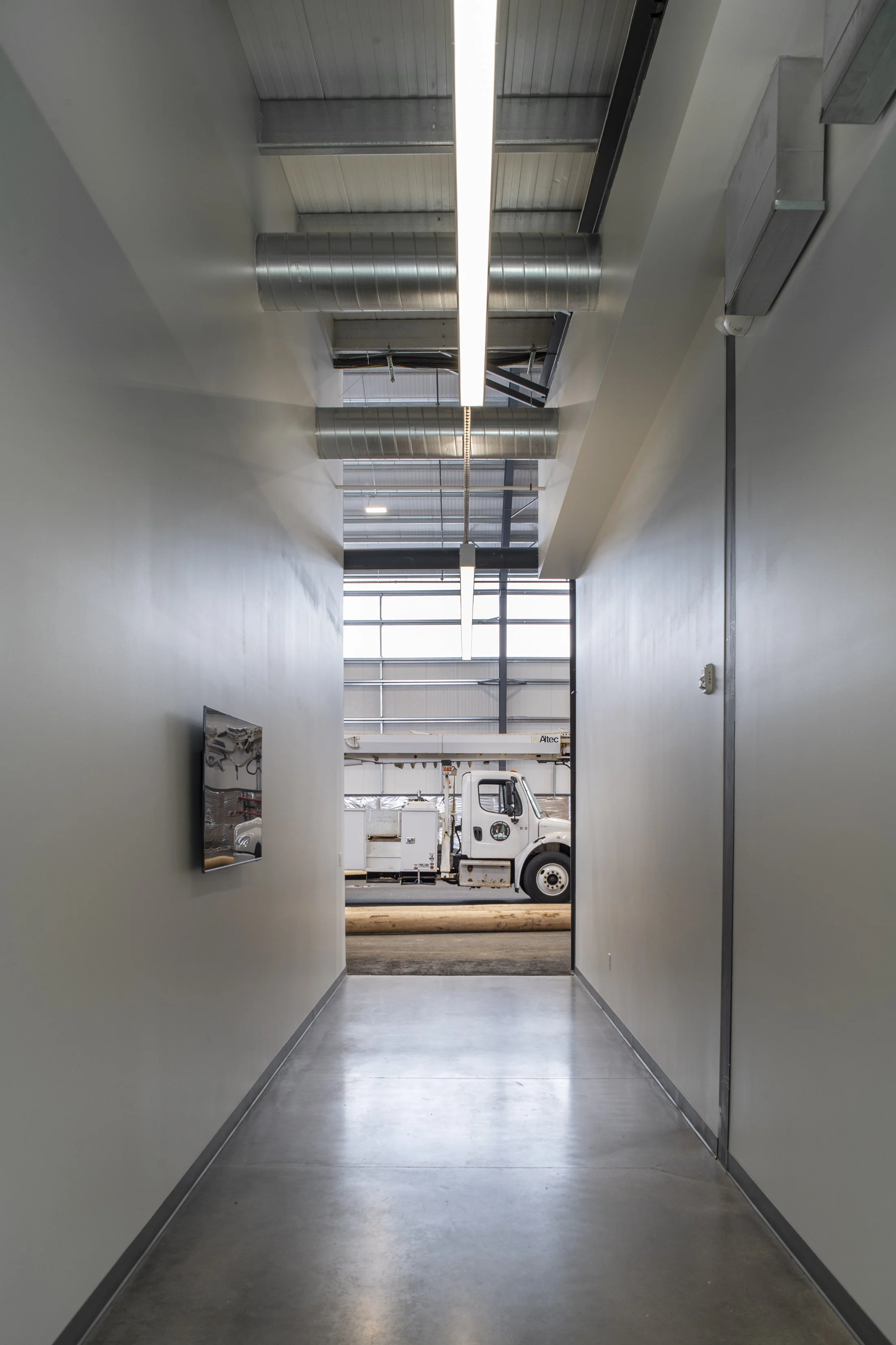 Indoor hallway leading to a garage or warehouse with a large white utility truck visible outside through the open door.