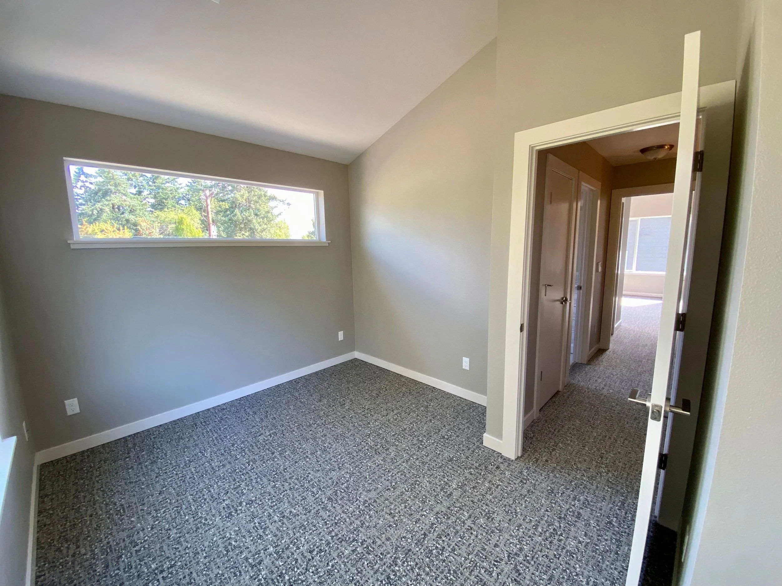 Empty room with gray walls, a long horizontal window, and an open door leading to a hallway.