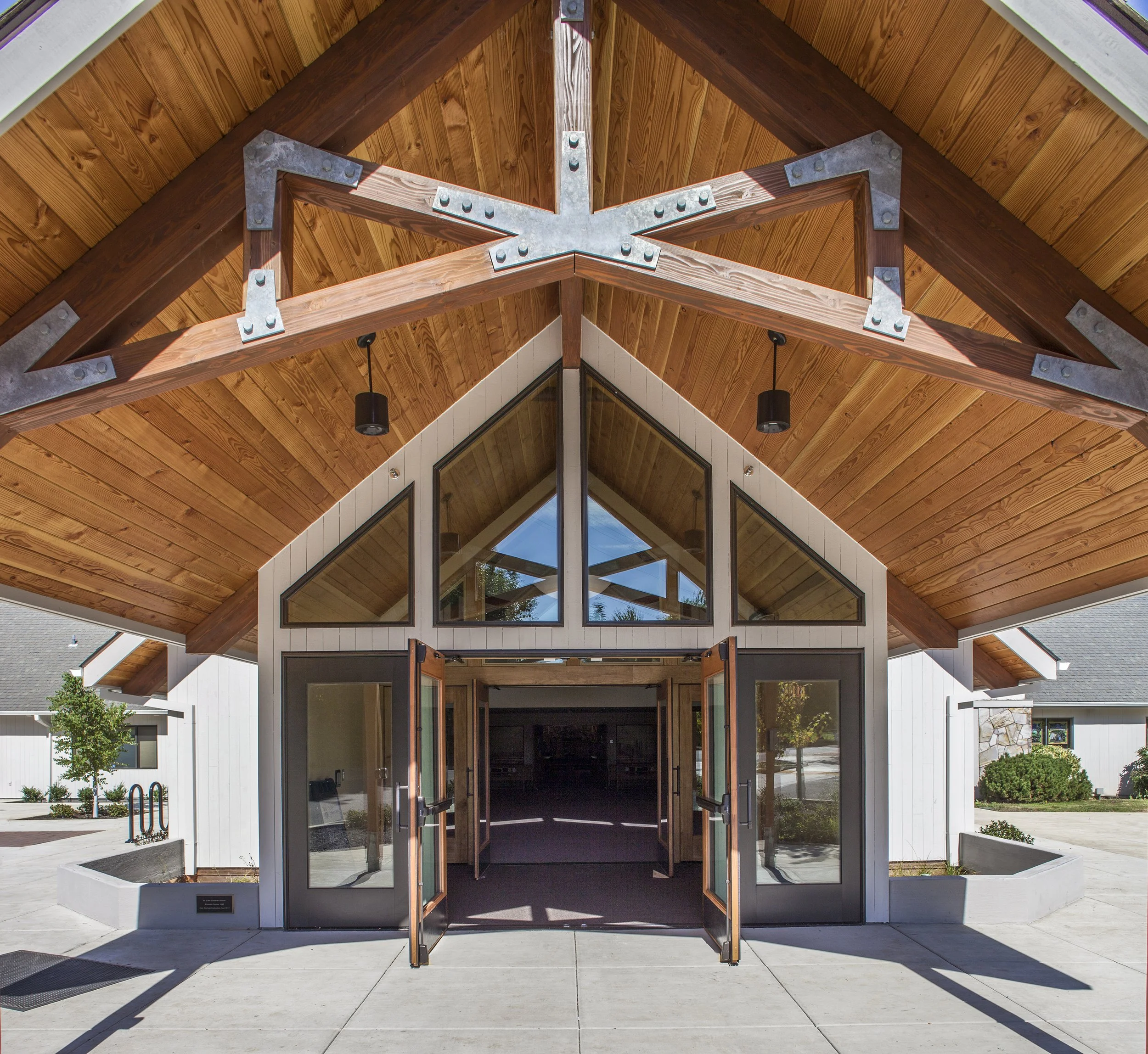 Entrance to a modern building with folding glass doors, a high peaked wooden ceiling with metal accents, and large triangular windows.