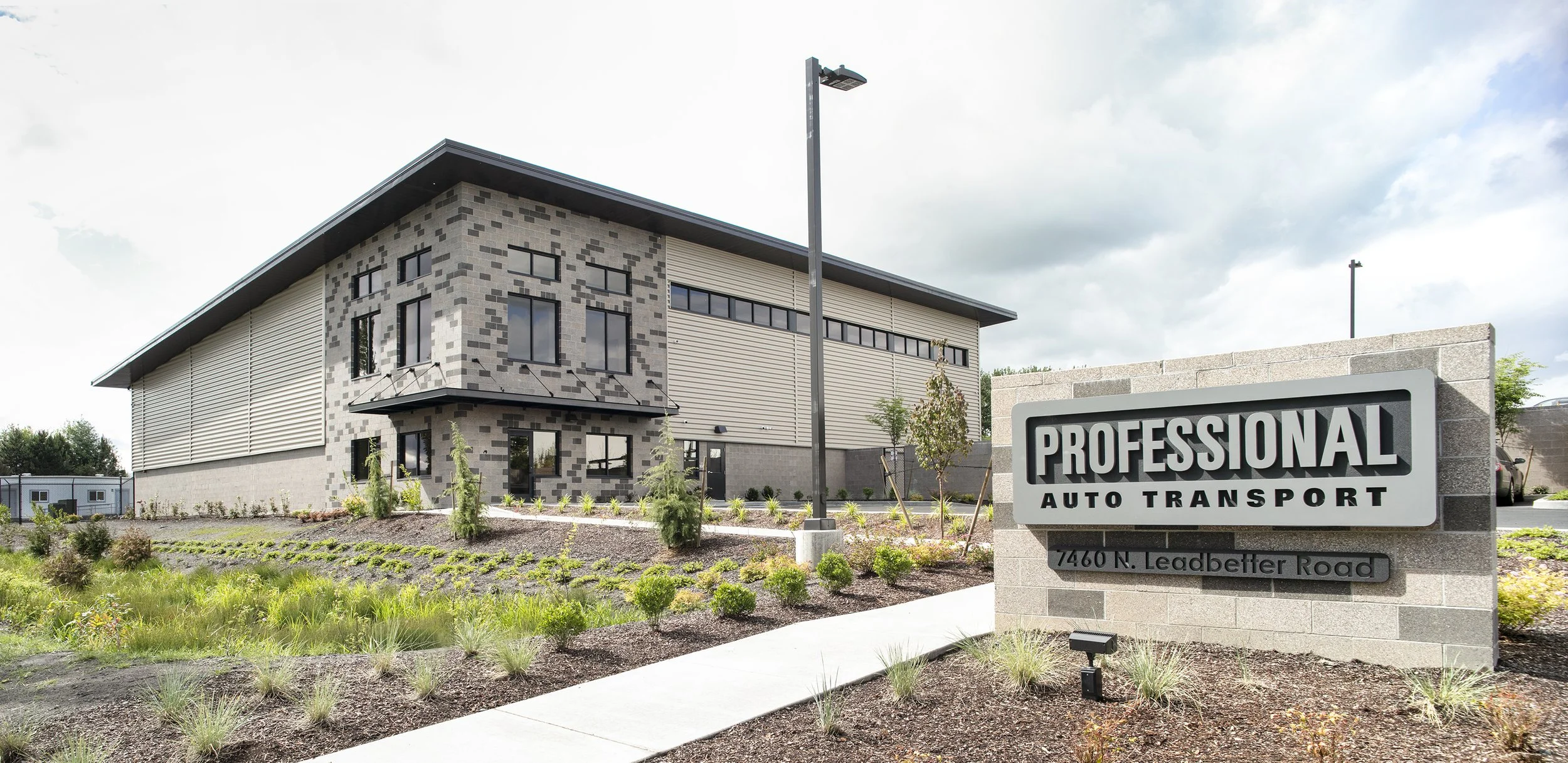 A modern commercial building with a landscaped front yard and a large sign reading 'PROFESSIONAL AUTO TRANSPORT,' located at 7460 N. Leadbetter Road.