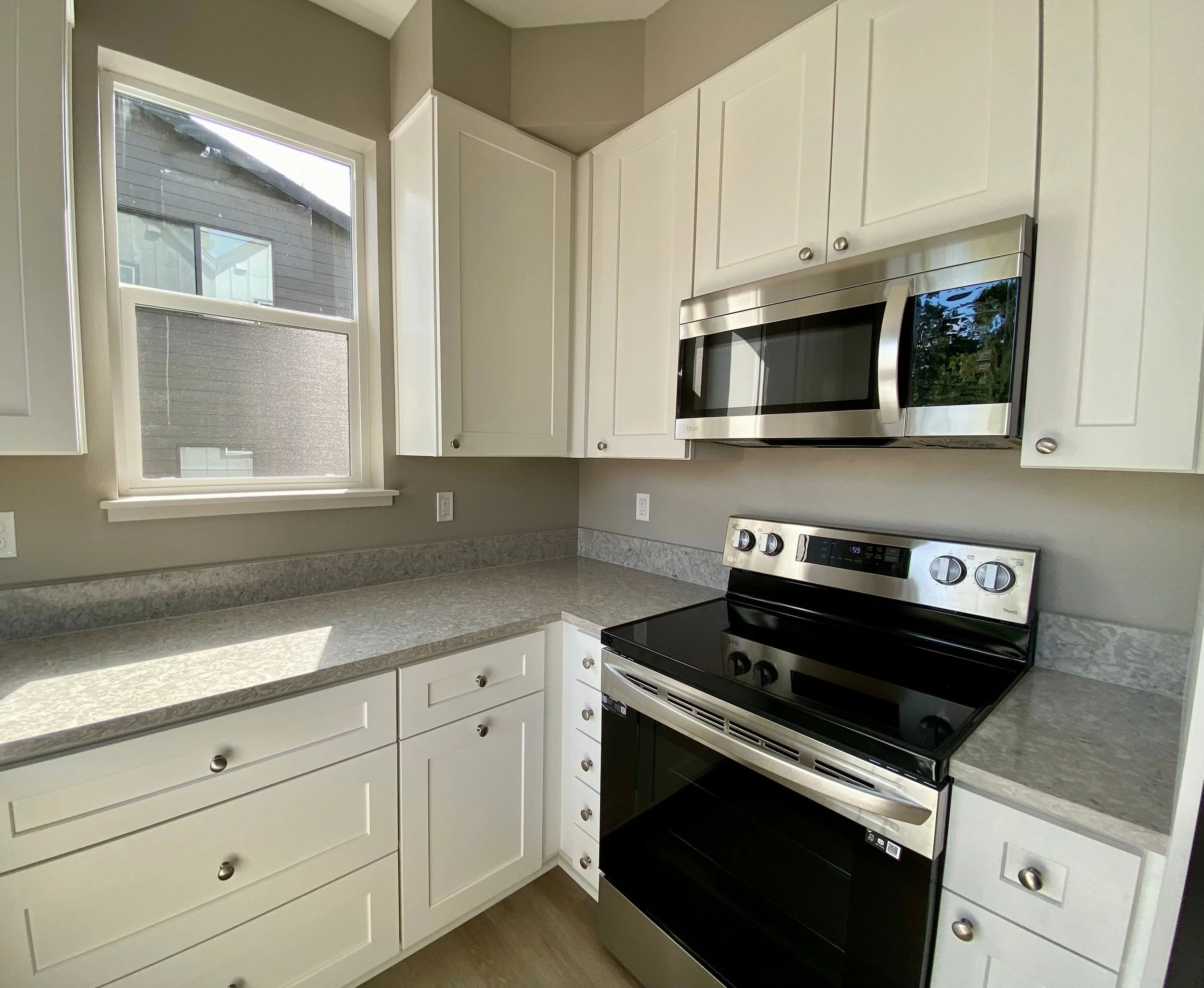 Modern kitchen with white cabinets, gray countertops, a window, a stainless steel microwave, and an electric stove.