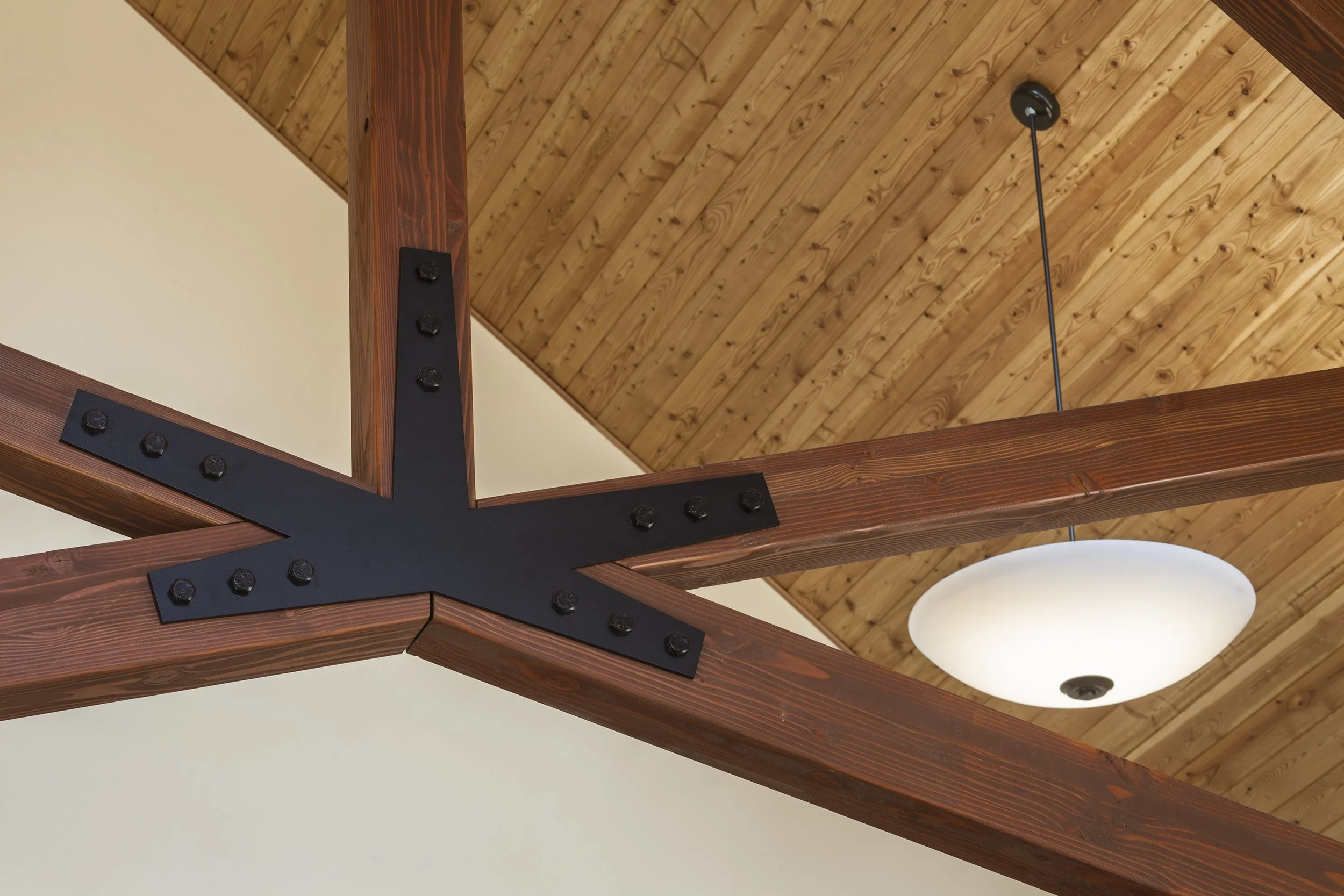 Interior ceiling with wooden beams, metal brackets, and a round ceiling light.