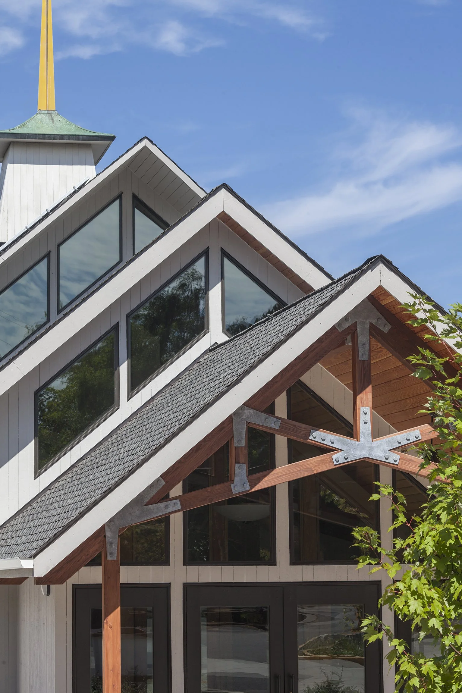Modern residential building with large triangular windows, wooden beams with metal brackets, and a peaked roof.