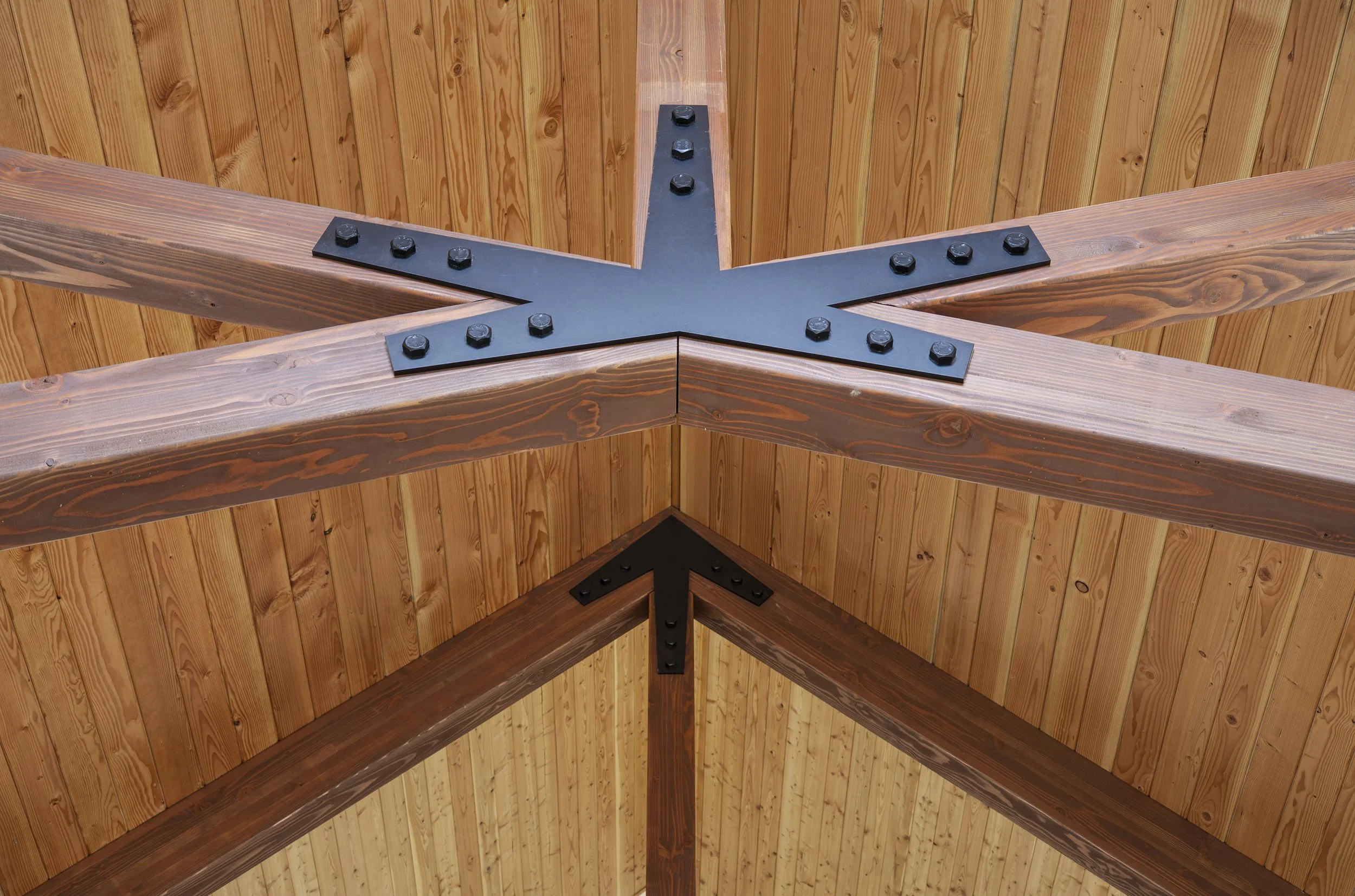 Close-up of a wooden ceiling with black metal brackets securing the beams at a pointed corner.