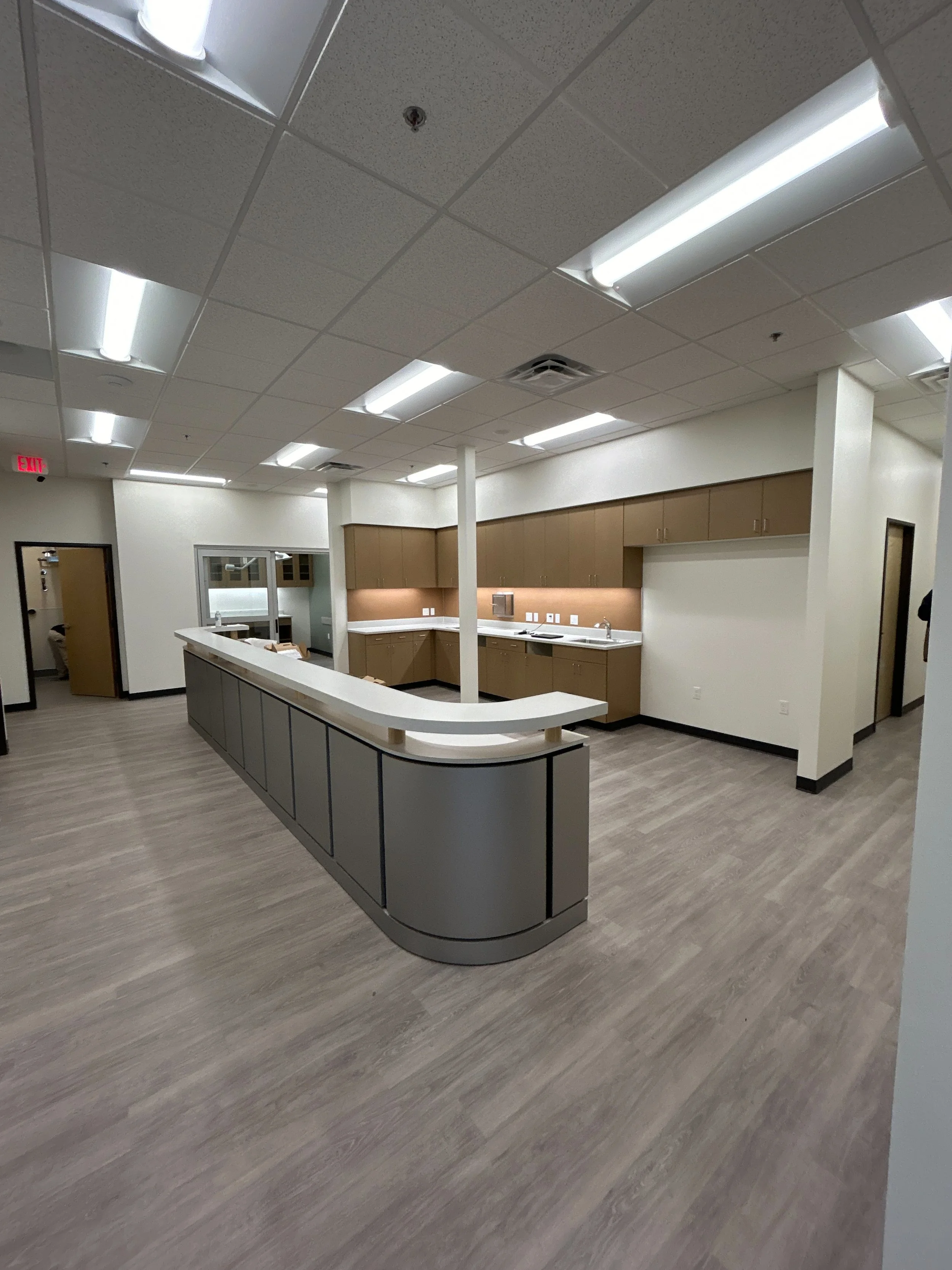 Empty medical or office break room with a curved countertop, brown cabinetry, and ceiling lights.