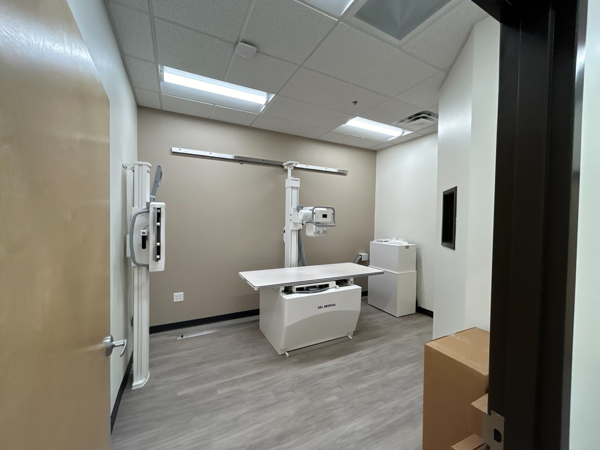 Empty medical X-ray room with X-ray machine, table, and viewing monitor.