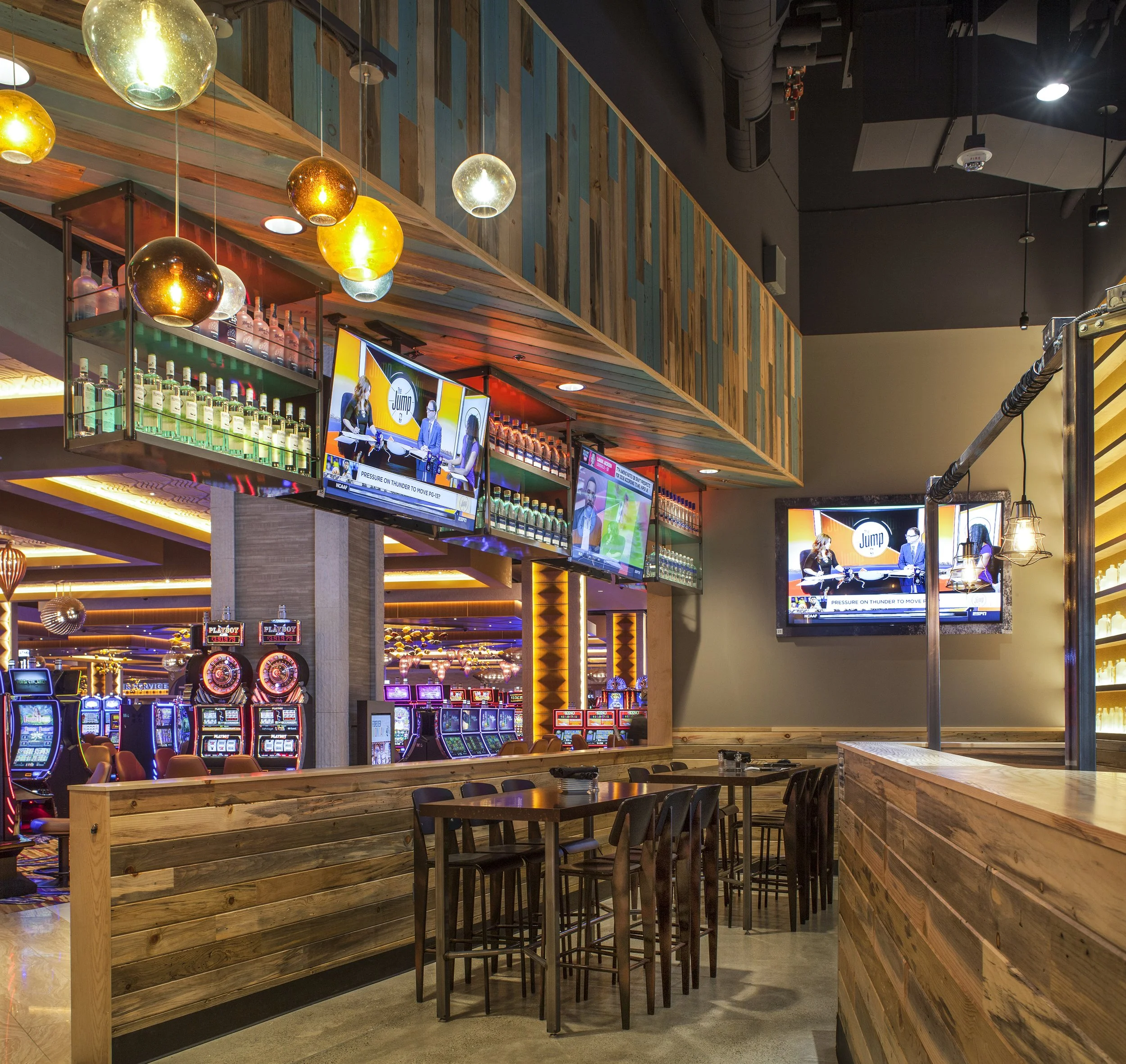 Inside a modern casino or bar with slot machines, multiple TVs, and wooden decor.