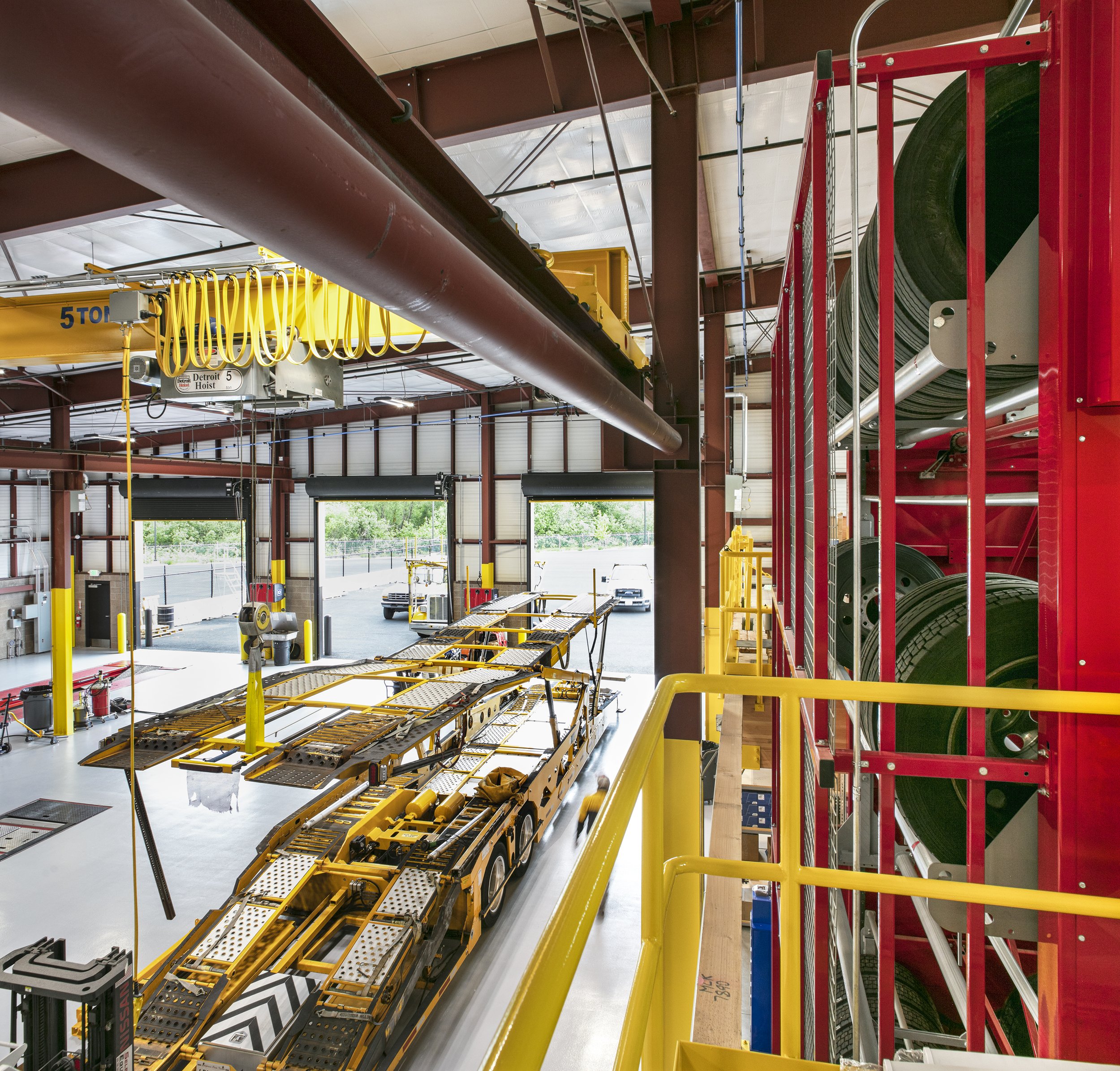 Inside a fire station with a large yellow crane, a red rack of fire hoses, and a yellow mobile platform with equipment.