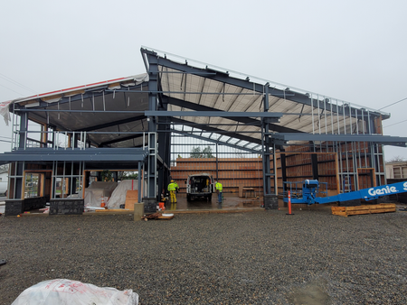 Construction workers and a vehicle on a partially built multi-story steel structure under rainy weather.