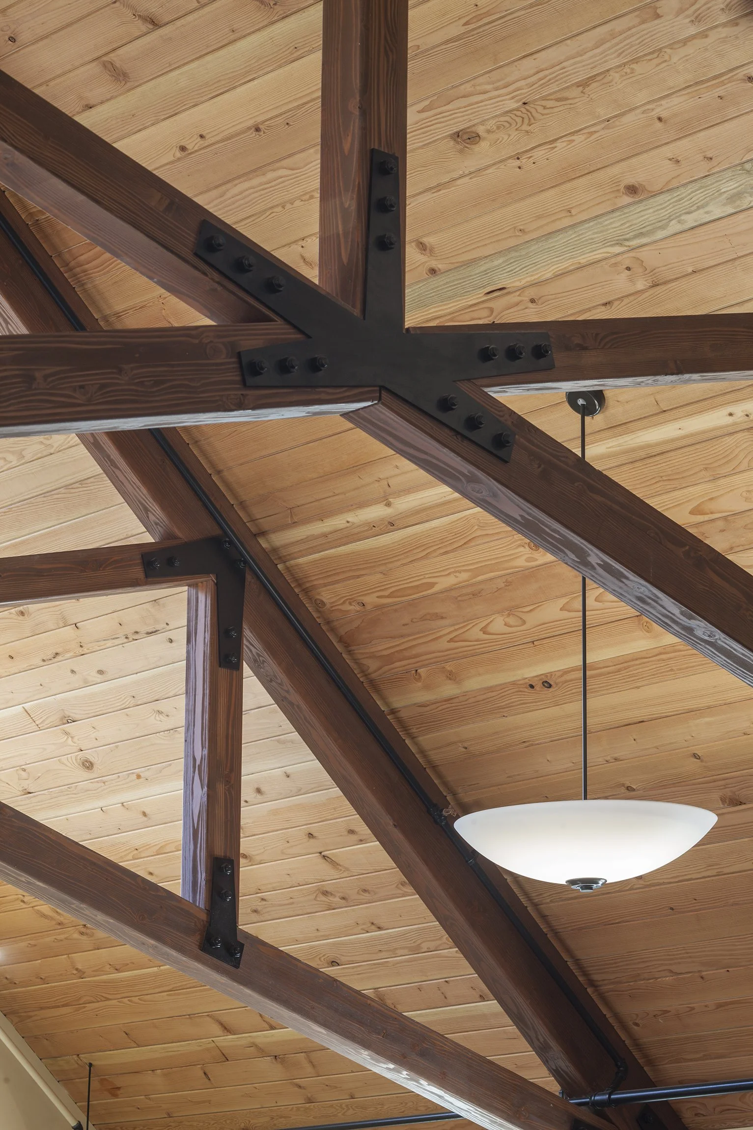 Close-up of wooden ceiling beams with black metal brackets and a hanging white dome light fixture.