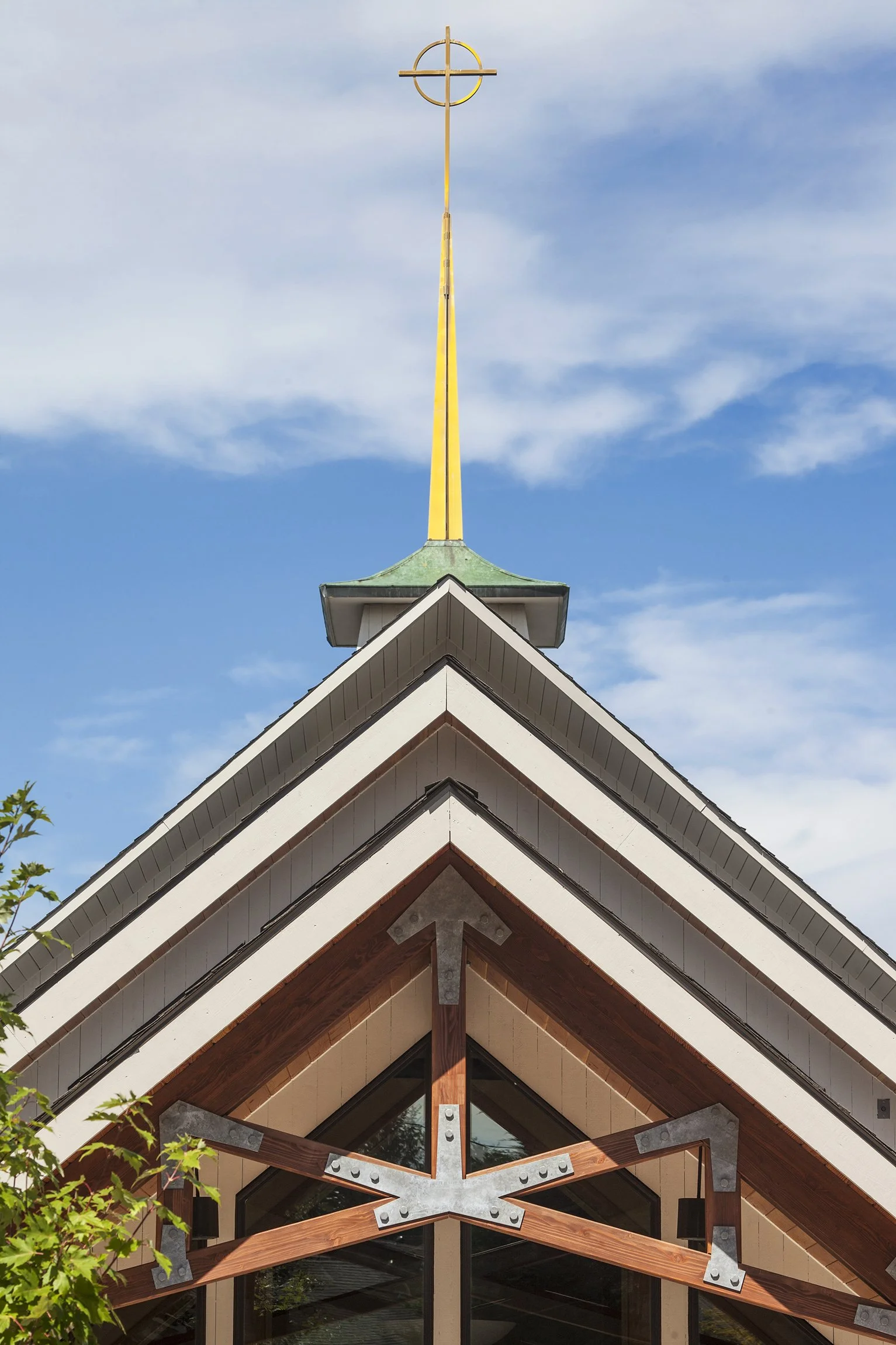 Close-up of church roof with a cross at the top against a blue sky with clouds.